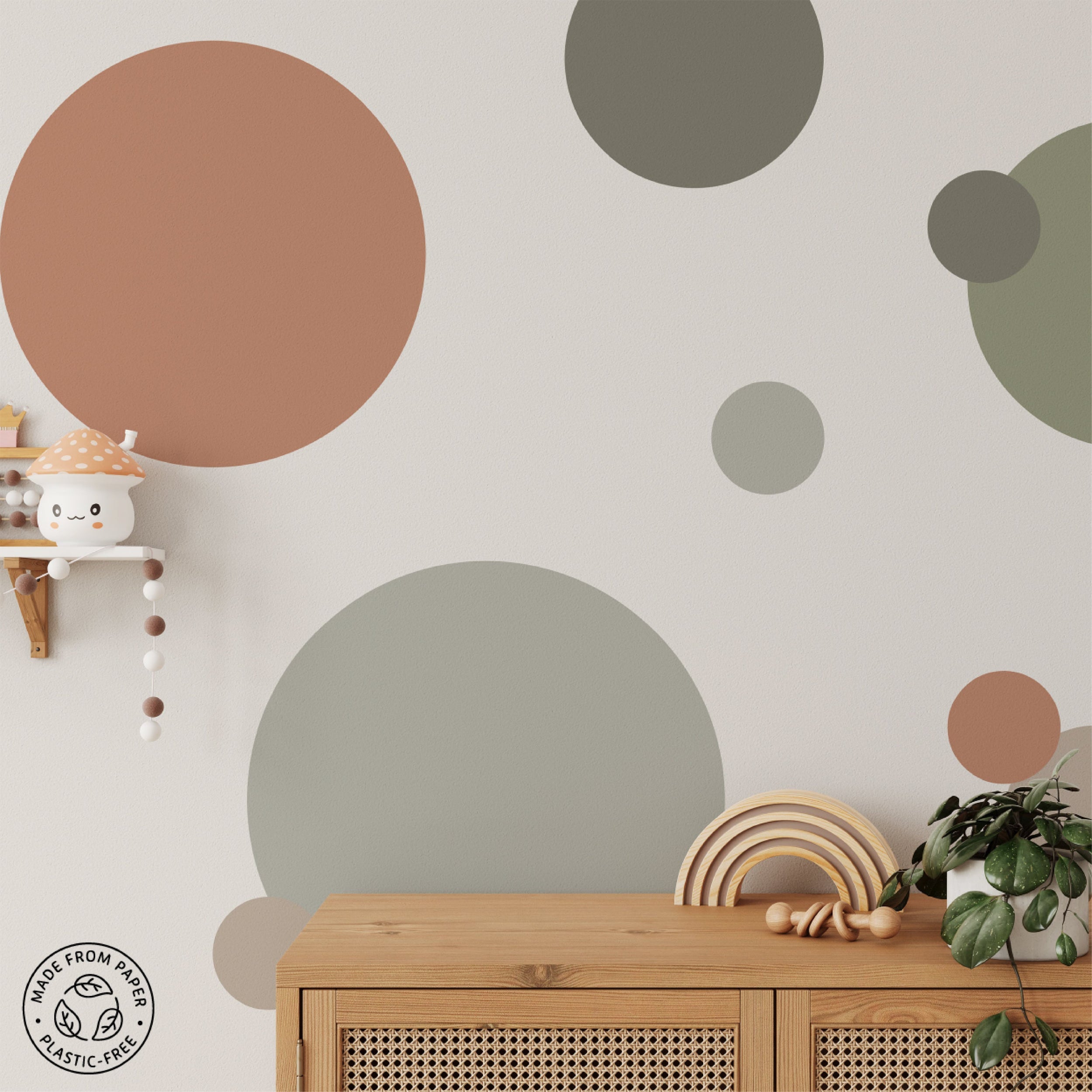 Minimalist nursery room with large pastel polka dot wall decals, a stuffed toy on a hanging shelf, a wooden rainbow, and a wicker cabinet. Made from paper, plastic-free badge in the corner.