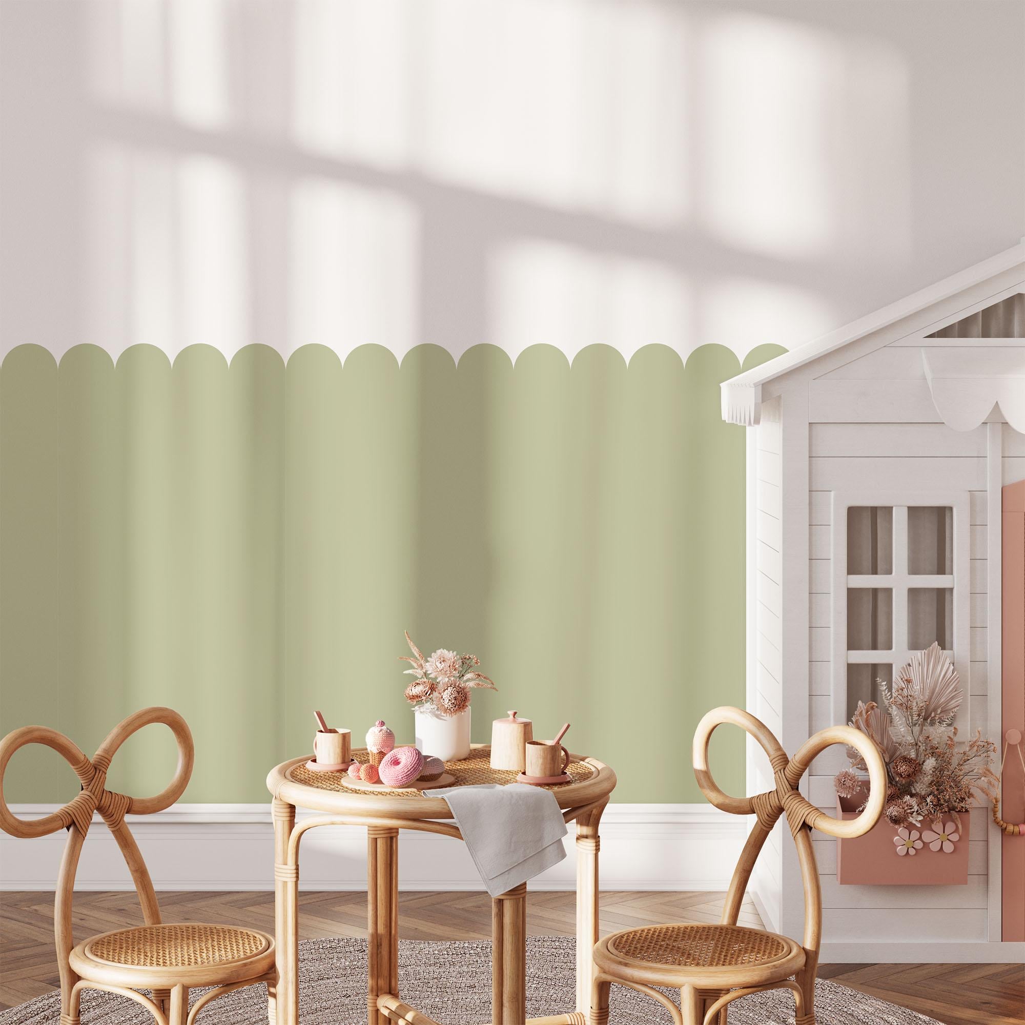 A childrens playroom with a small table set for tea, including pastel-colored cups and plates. Two whimsical chairs surround the table. A dollhouse and scalloped wall decor are in the background.