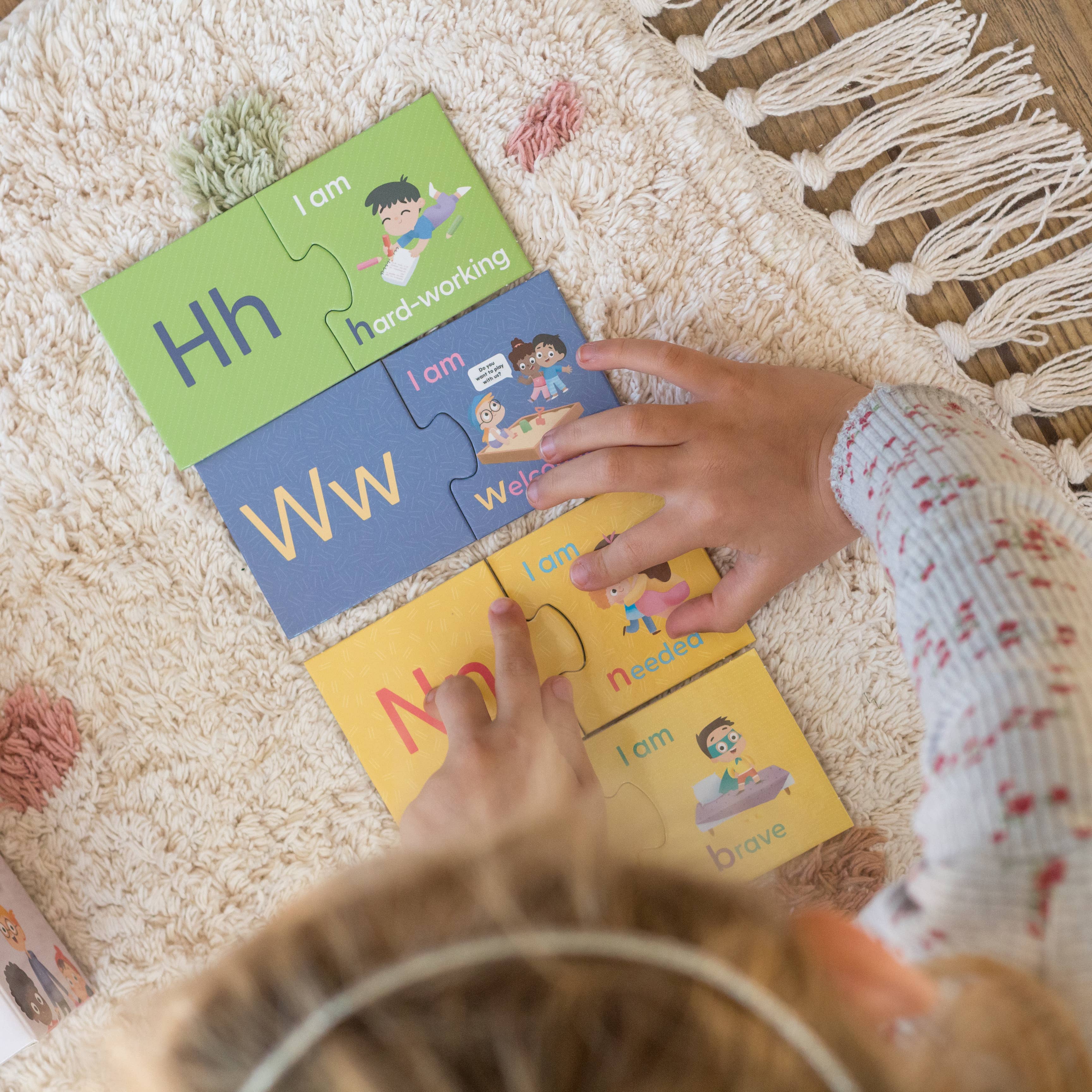 A child assembles the Mindful Champs 'A-Z I Love Me' Affirmation Puzzle, joining colorful pieces with letters and words like "hard-working" and "welcome," promoting a positive self-image through cheerful illustrations.