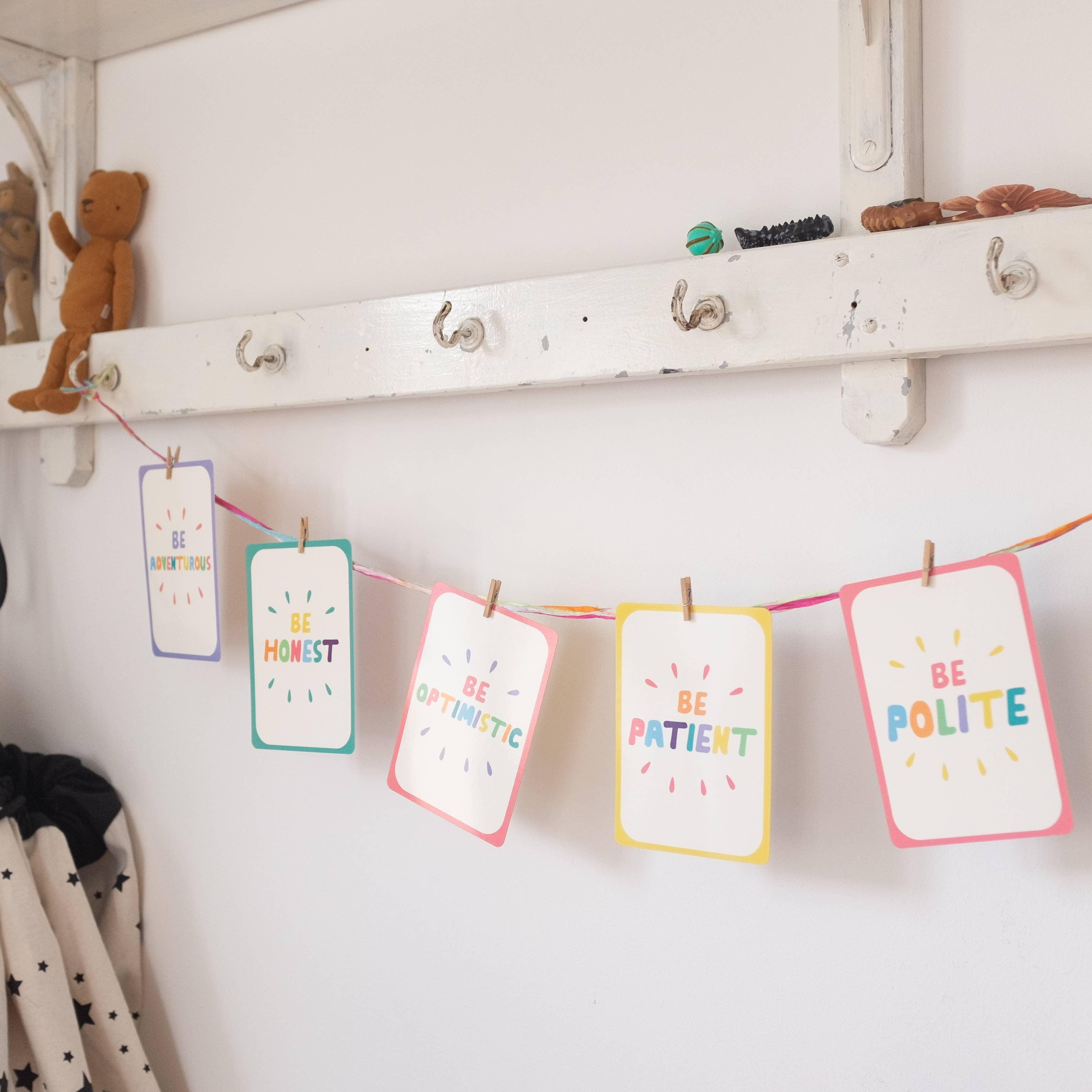 Mindful Champs Character Matters Flashcards for Kids with positive messages—Be Honest, Be Optimistic, Be Patient, and Be Polite—hang on a string with clothespins below a shelf to inspire character growth in children.