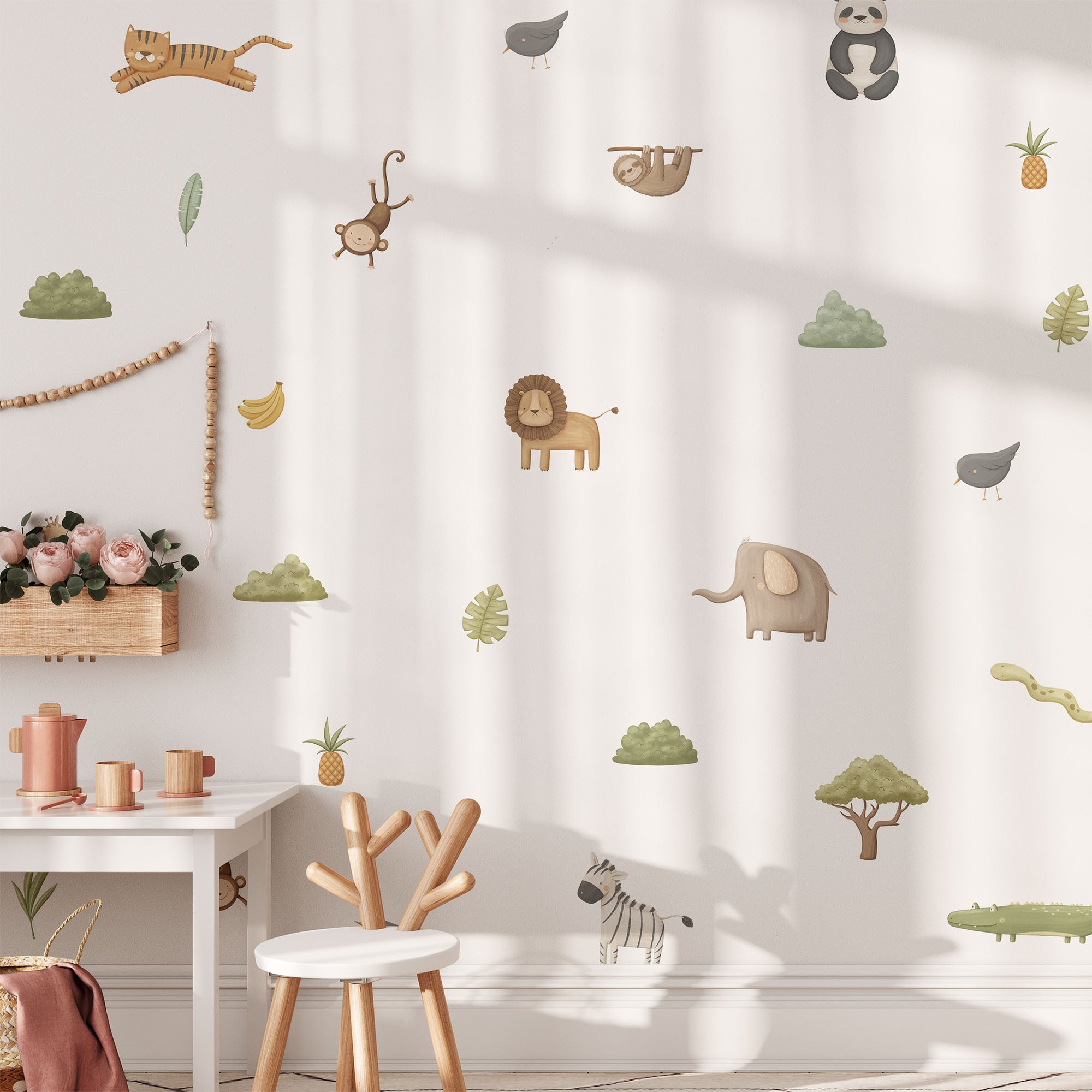 A childrens room adorned with My Stores Safari & Jungle Animal Stickers, featuring a tiger, monkey, sloth, lion, elephant, zebra, and panda. Below the wall decals is a white desk with a wooden chair beside pink flowers and nursery decor.