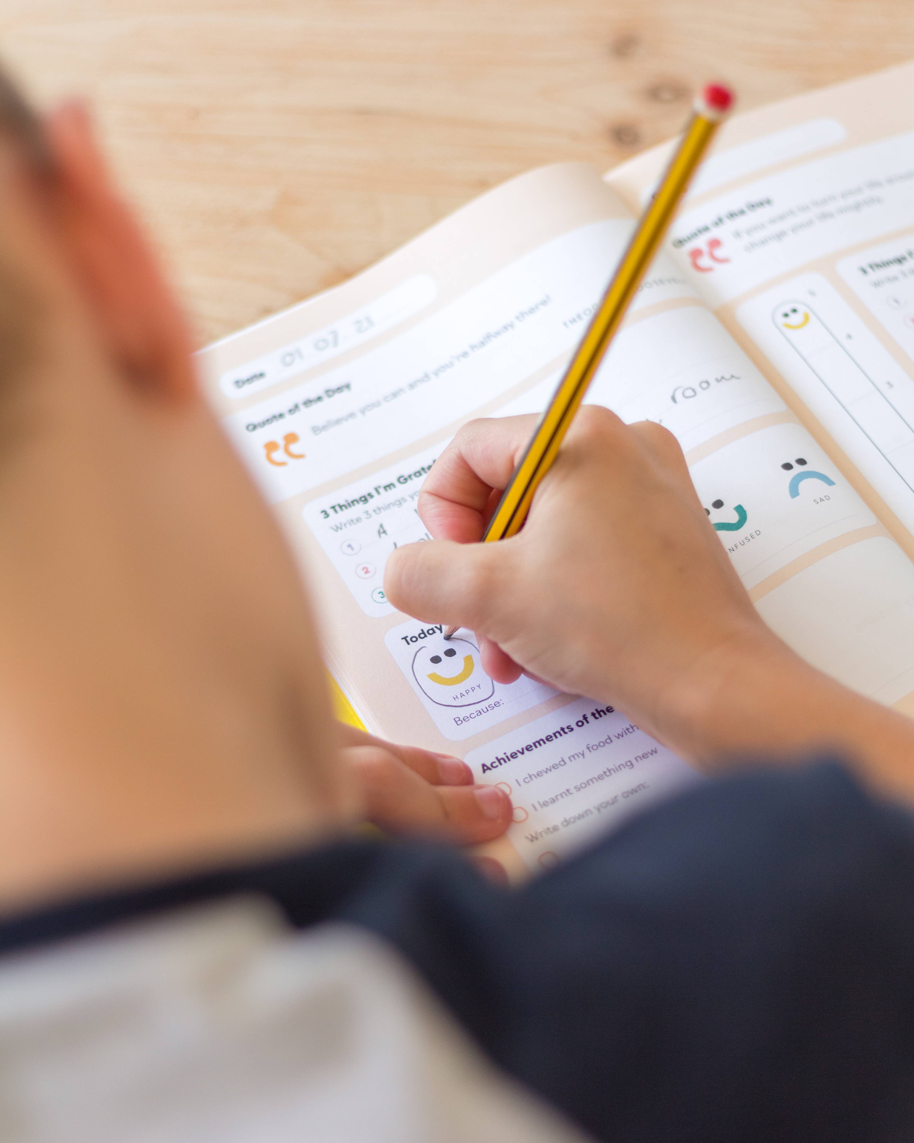 A child uses a yellow pencil to fill out prompts and draw in the open "My Mindful Me Journal" by Mindful Champs, focusing on gratitude and mindfulness practices.
