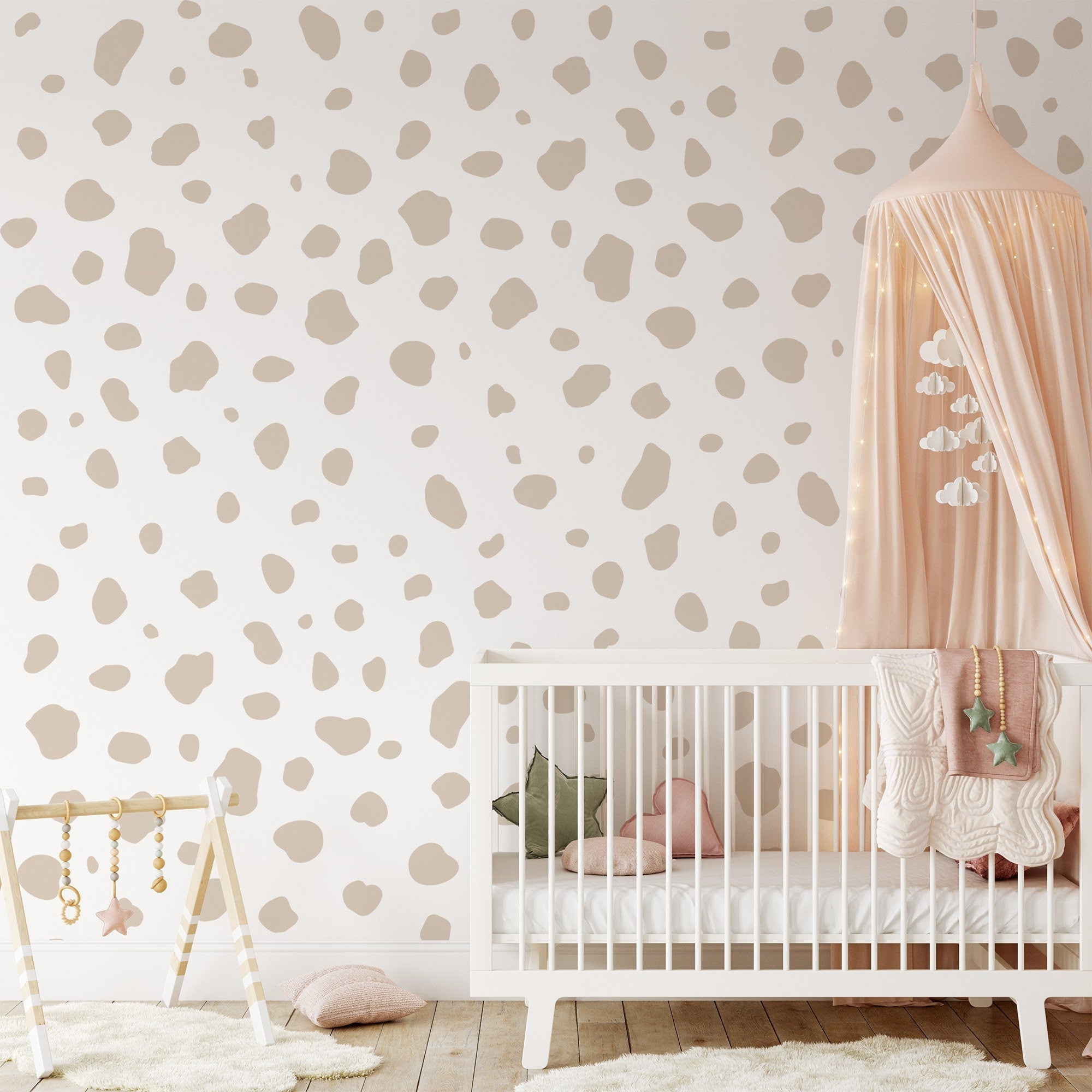 A cozy nursery showcases a white crib with pastel bedding and a pink canopy with hanging stars. The wall is adorned with My Stores Dalmatian Spot Large Stickers. A baby gym featuring hanging toys sits in the foreground, with soft toys scattered on the floor.