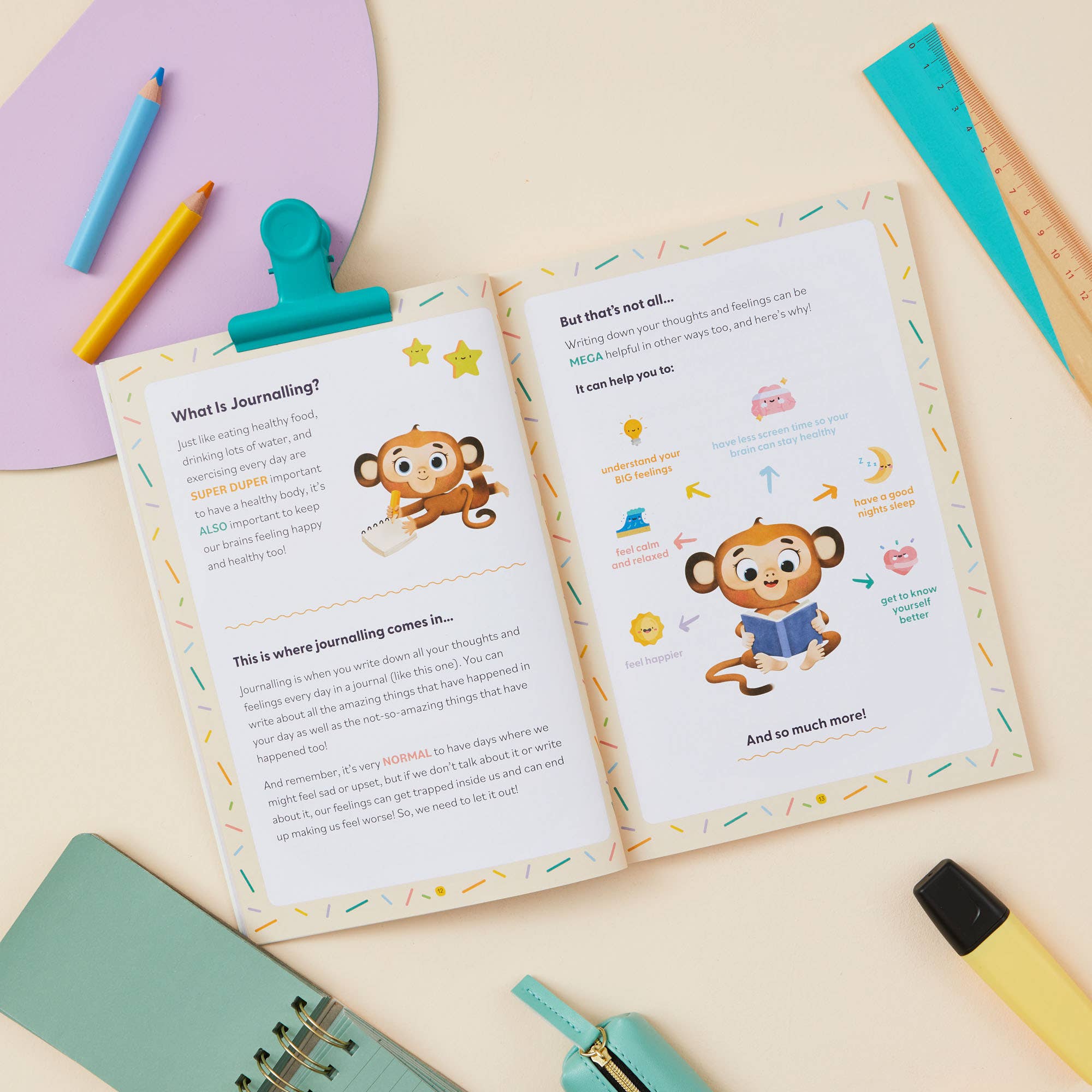 The My Mindful Me Journal Early Years Edition by Mindful Champs lies open on a desk, its playful monkey illustrations and easy text introducing kids to journaling. Colorful pens, a ruler, and a teal notebook surround the book.