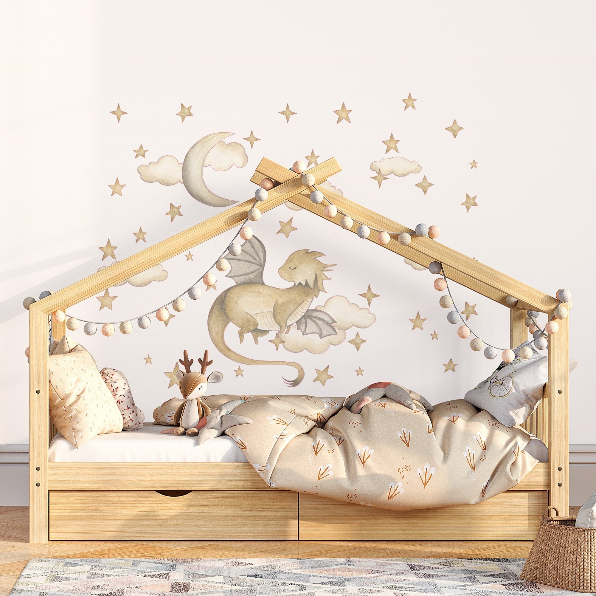 A childs bed shaped like a house boasts plush bedding and a stuffed deer toy, with star, moon, and My Stores Golden Dragon Stickers on the wall above. A string of pom-pom lights adorns the wooden frame.