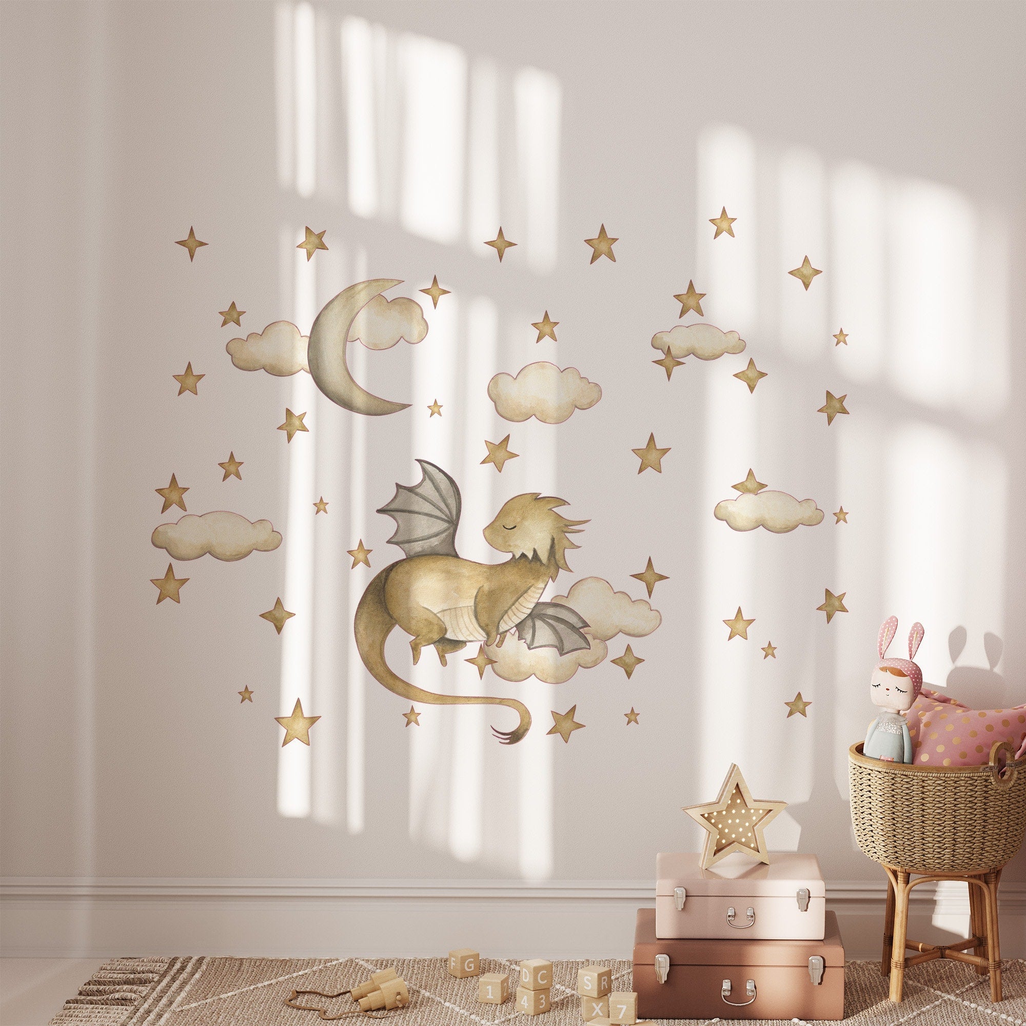 A nursery room showcases My Stores Golden Dragon Stickers depicting a dragon among clouds, stars, and a moon. A basket holds a stuffed rabbit beside star-topped suitcases on the floor, while soft lighting adds coziness.