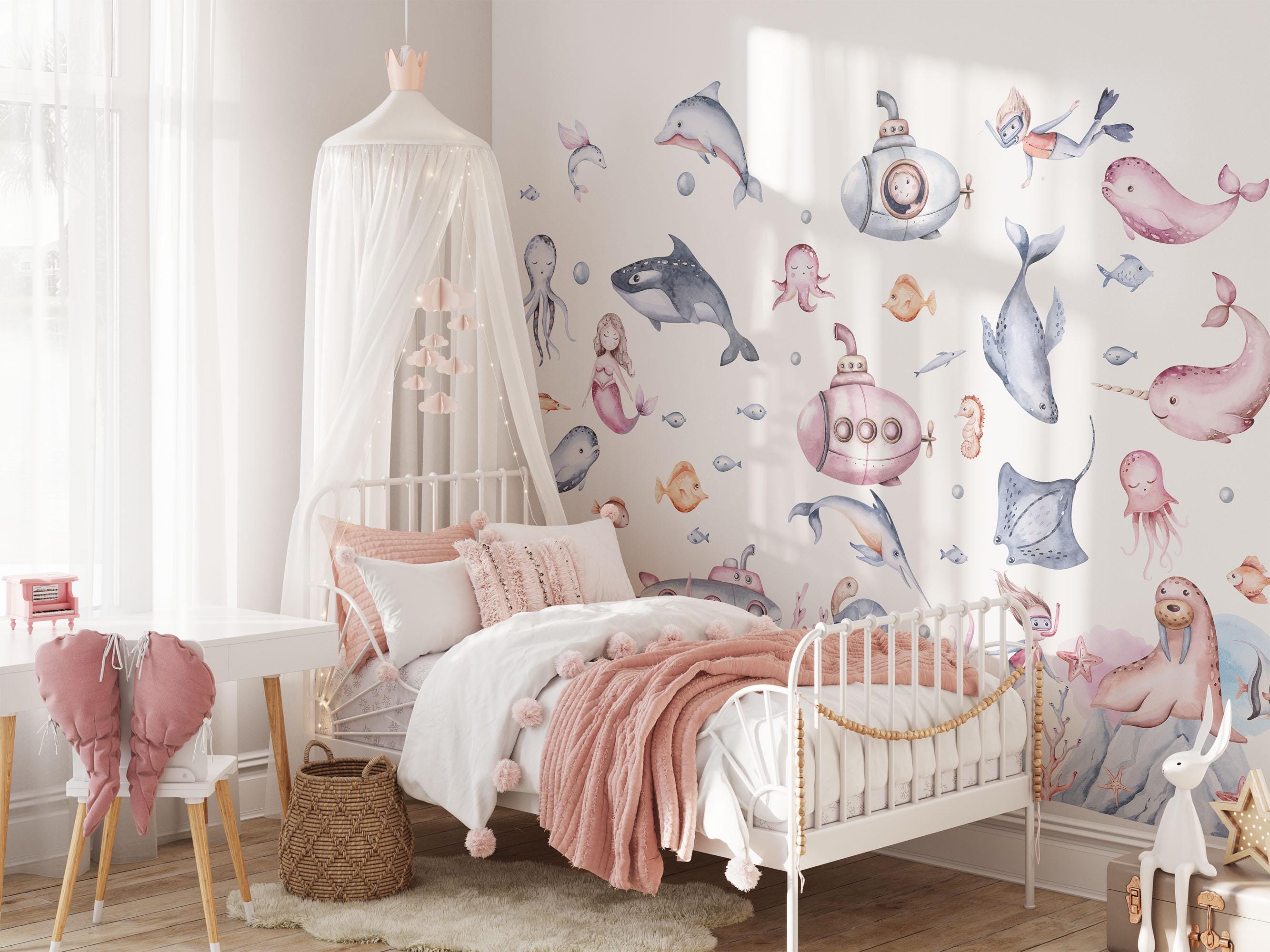 A delightful childrens bedroom adorned with My Stores Under The Sea Nursery Wall Stickers, showcasing whales, a submarine, and sea creatures. It features a pink canopy bed, soft pillows, a stuffed animal, and a small desk with chair. Light pours in through the large window.