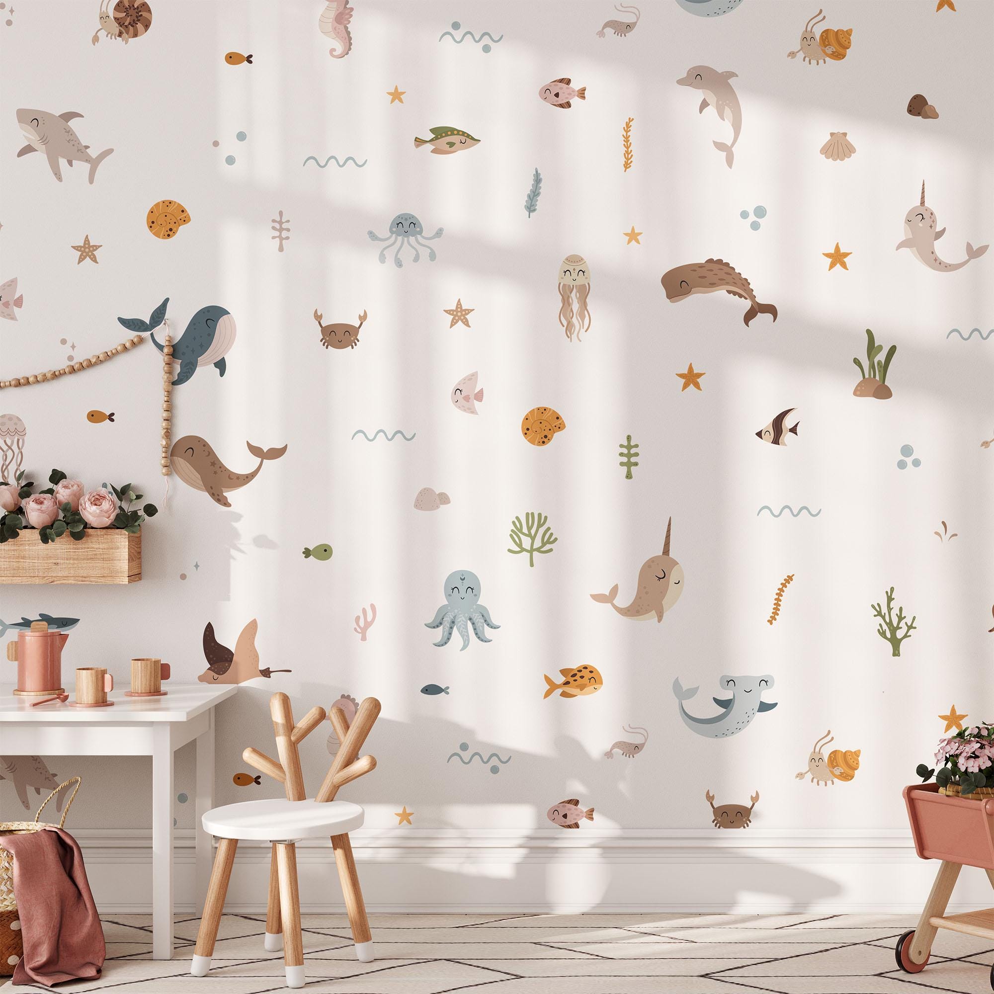 A childrens room with a sea-themed wall design features My Stores Ocean Animals Stickers, including dolphins, narwhals, and fish that adorn the white wall. A chair, small round table, and vase with flowers add to the cozy decor as soft sunlight filters in.