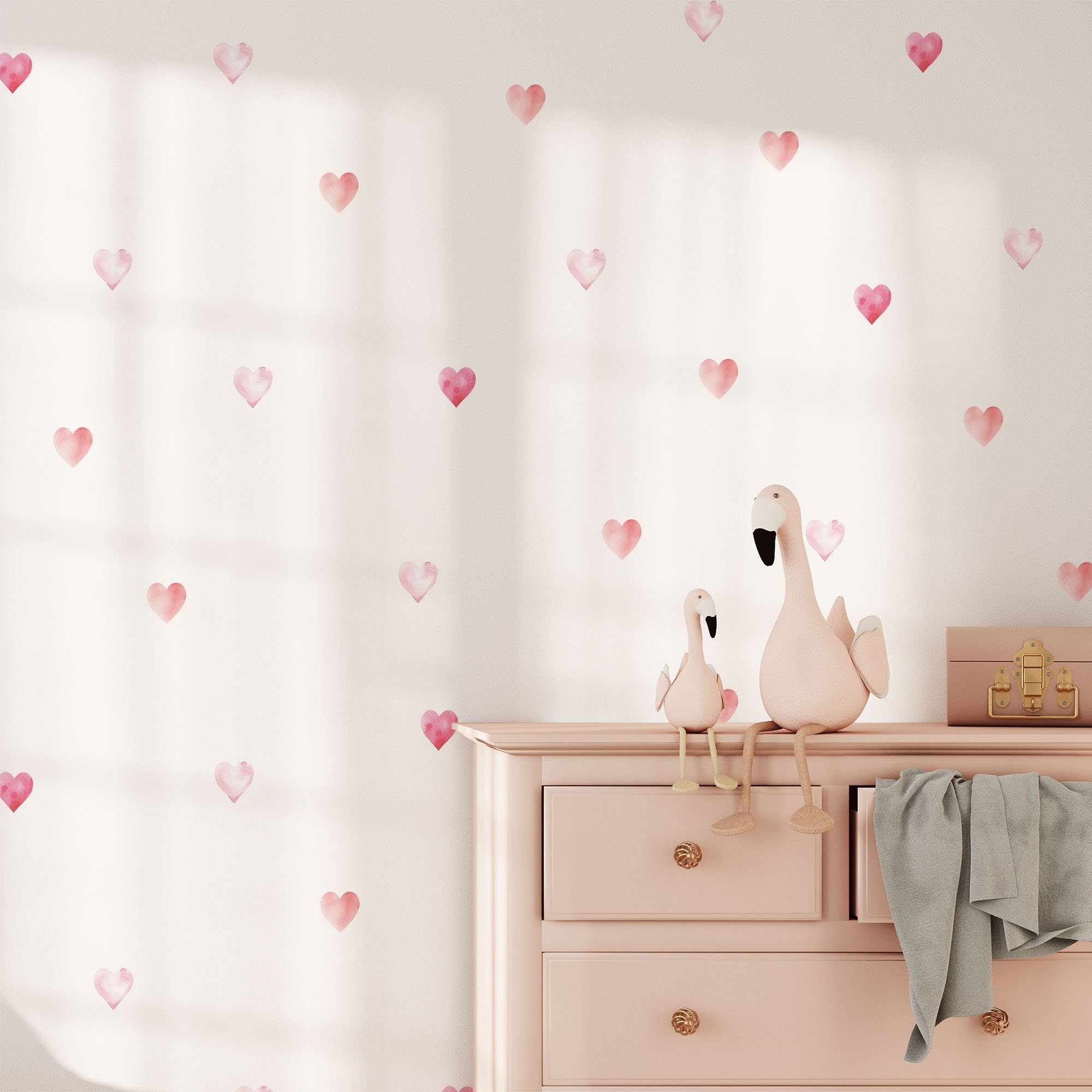 A pink dresser featuring two stuffed birds (one large, one small) is adorned with a light blue blanket. The My Store Watercolour Heart Stickers on the wall behind are complemented by sunlight that casts charming shadows on these artistic decals.