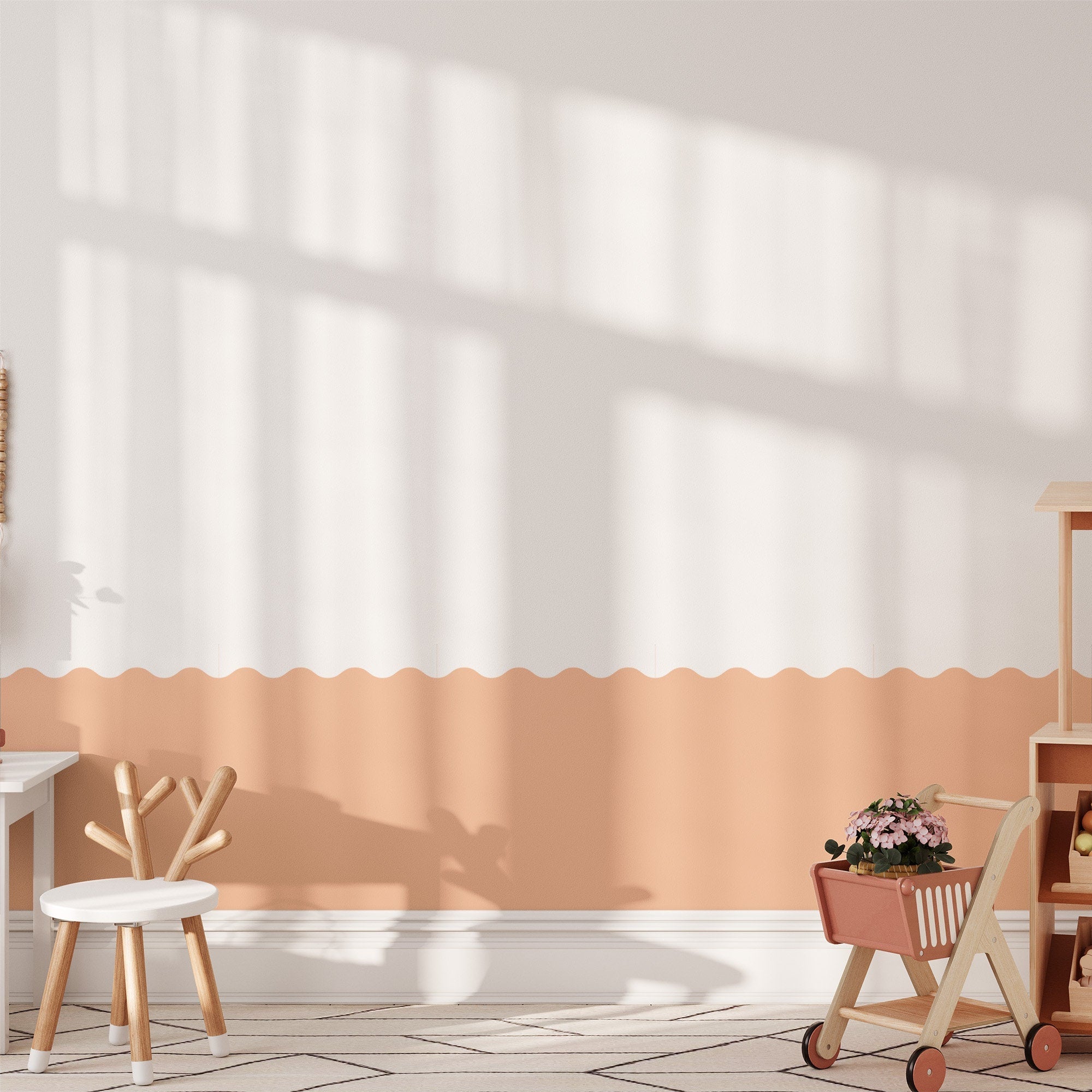A cozy childrens playroom with soft white and peach walls, adorned with My Stores Wave Wall Stencil. Sunlight creates patterns through the window, complemented by a small white table and chair, a wooden toy shopping cart with flowers, and a patterned rug.