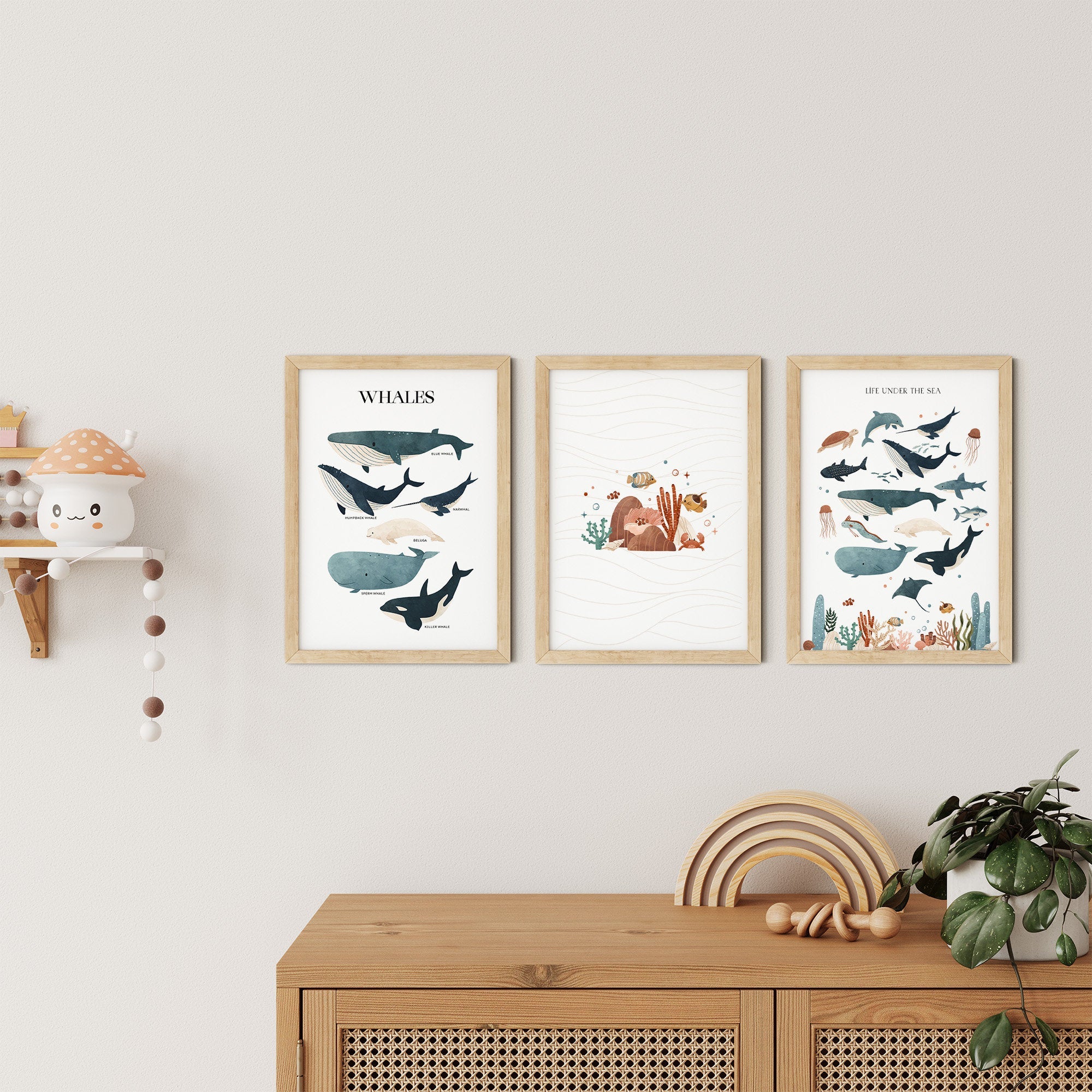 Three Sea Animals Nursery Prints by My Store adorn the wall—one with whales and another showcasing vibrant sea creatures, including dolphins. Below, a wooden cabinet holds stacked rings and a plant, complemented by mushroom-themed nursery art on a shelf.