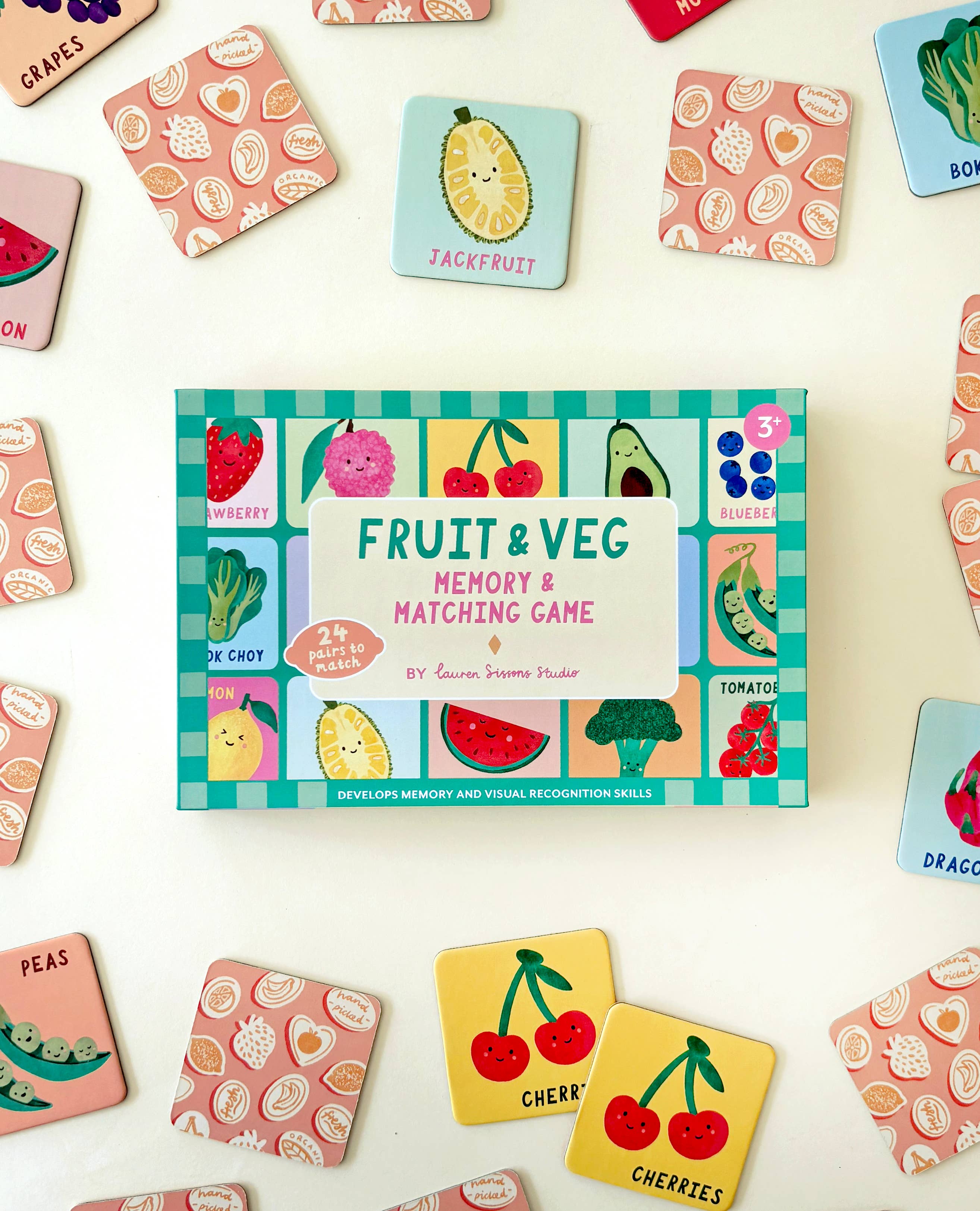 The Fruit and Veg Memory & Matching Game by Lauren Sissons Studio features a colorful box surrounded by illustrated cards of jackfruit, cherries, peas, and dragonfruit—a fun educational gift that makes learning enjoyable for kids.