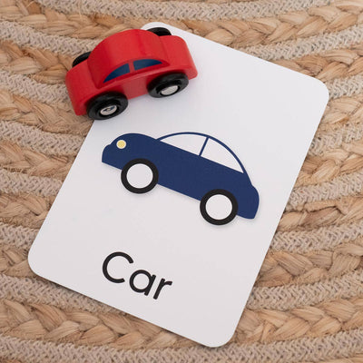 The Priya & Peanut First Word Flash Cards | 50 First Words For Toddlers set features a blue car card labeled "Car" on a textured surface, with a red toy car on top—ideal for playful learning and boosting toddler speech development.