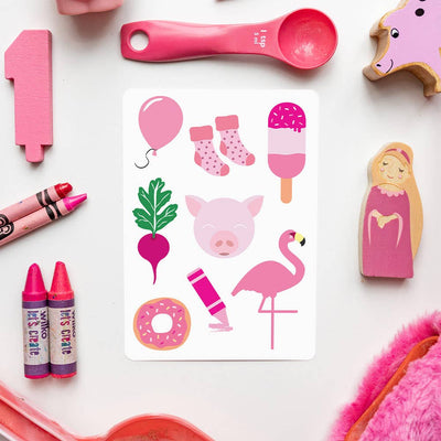 A Priya & Peanut Colour Flash Card featuring pink illustrations—pig, flamingo, balloon, ice cream, donut, crayon, beet, socks, and heart—is surrounded by pink toys and objects on a white surface.