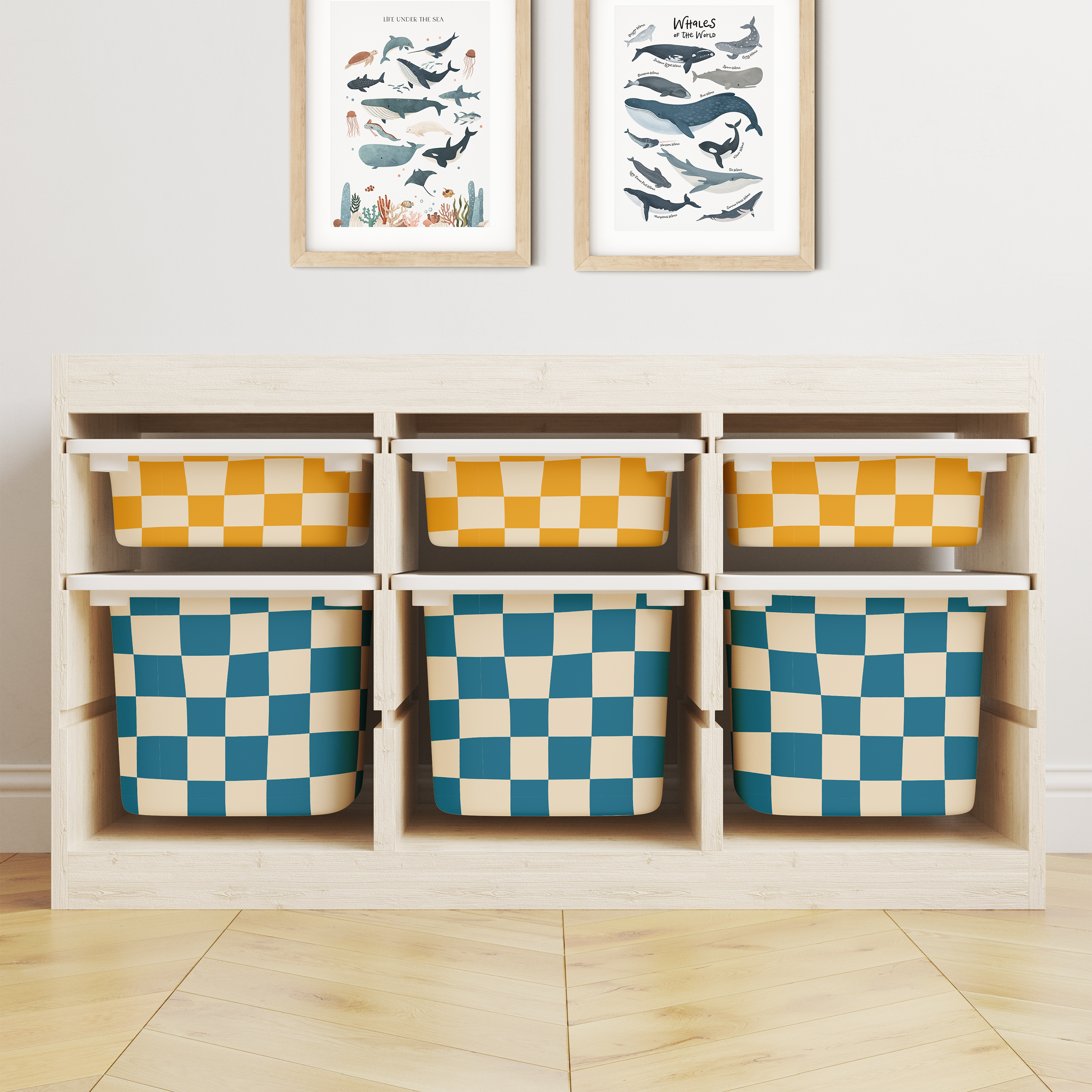 Wooden storage unit with six bins in a blue-and-yellow checkered pattern features Baby Belle's IKEA Trofast Checkered Box Stickers for a playful look. Above, two marine-themed prints hang over the light herringbone floor.