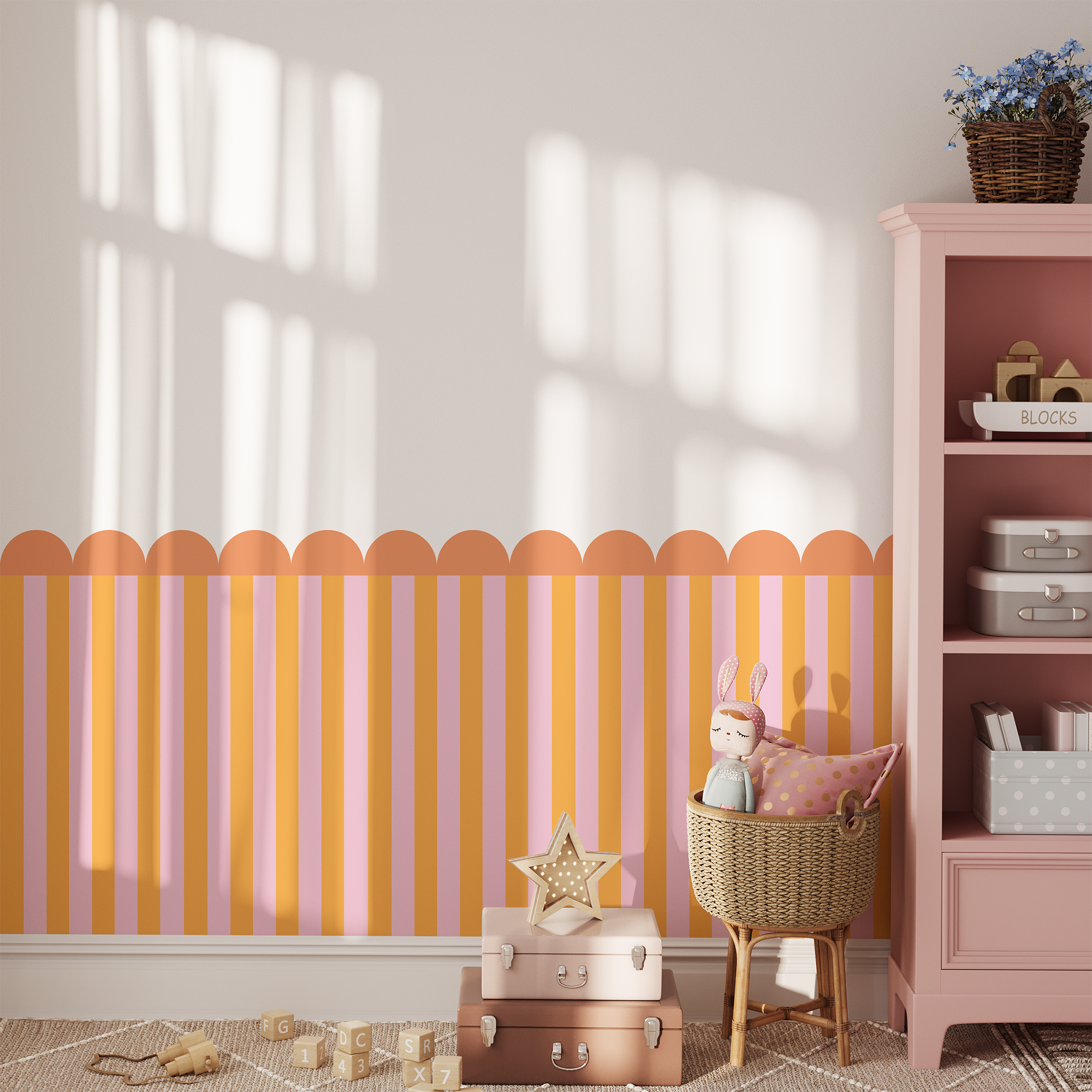 A sunlit kids' room features Benji & Belle’s Striped Half Wall Bespoke Wallpaper with scalloped trim, a wicker basket with a stuffed bunny, pink drawers, toys, and stacked suitcases on the wooden floor.
