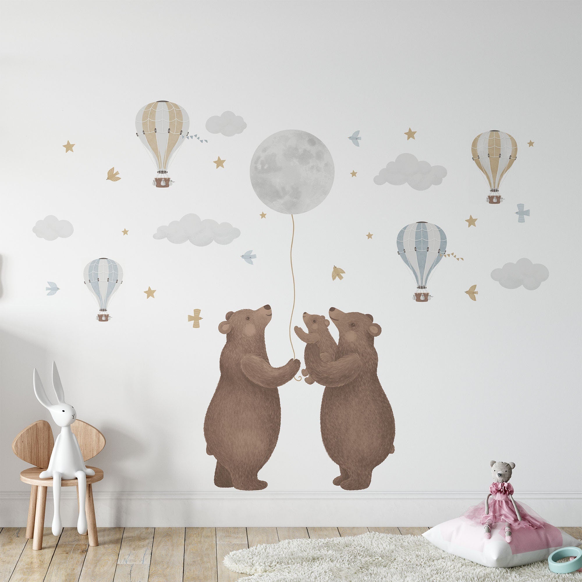 A childrens room features Bears & Moon Stickers by My Store, with three cartoon bears holding a balloon among clouds, stars, and hot air balloons. A small chair with a toy rabbit and plush bear on a cushion completes the dreamy scene.