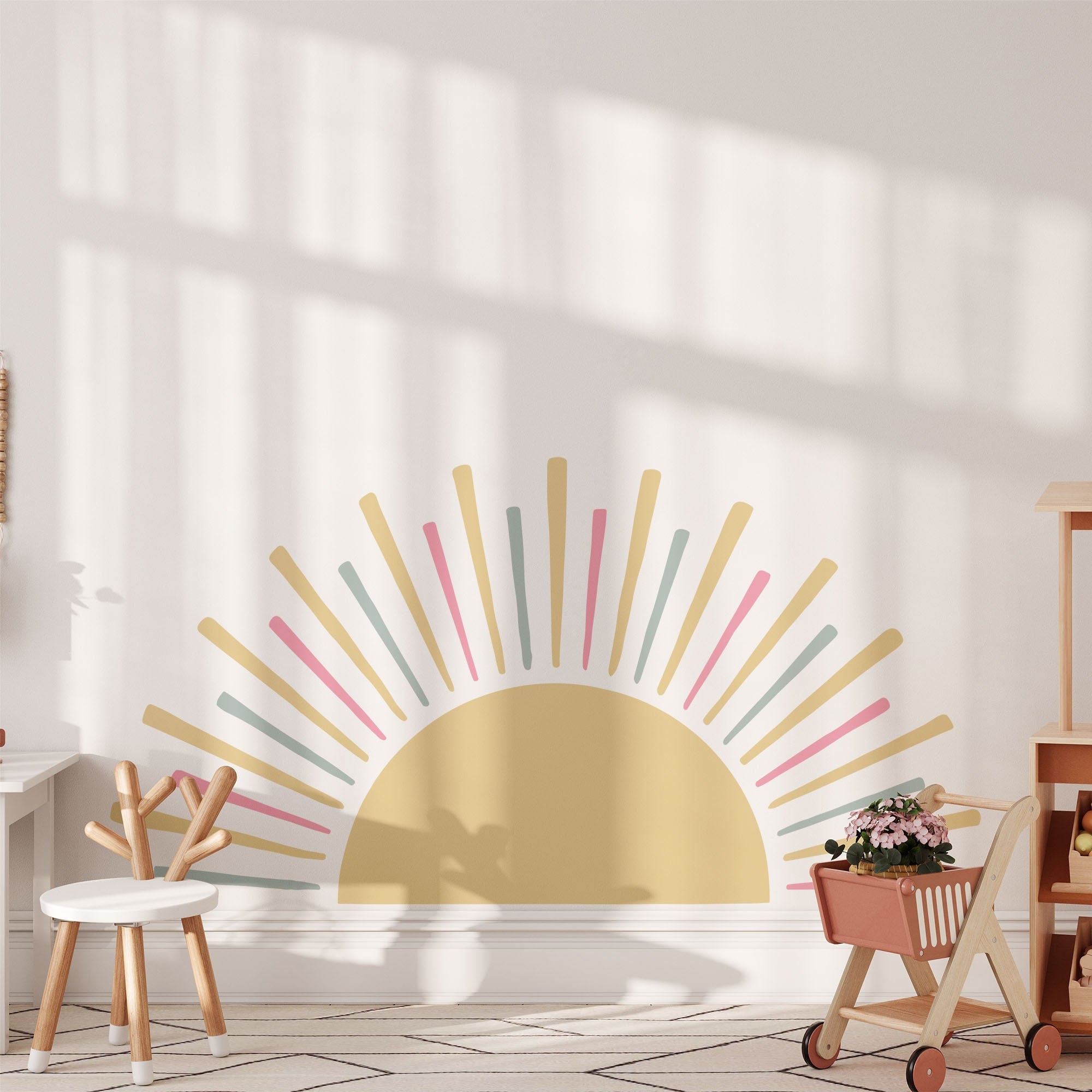 The Boho Sun Sticker by My Store brightens a childs room with cheerful yellow, pink, and green rays. Wooden chairs, a toy kitchen set, and a potted plant on a pink stroller add charm, all illuminated by sunlight through large windows. A perfect nursery decor piece!.