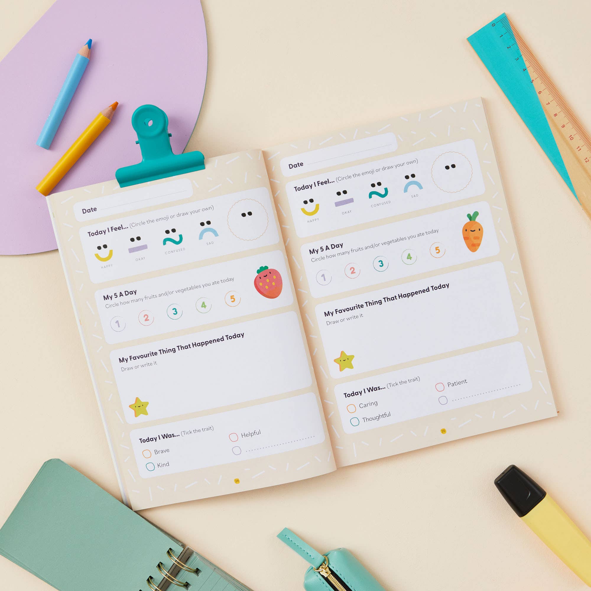 The My Mindful Me Journal Early Years Edition by Mindful Champs is an open mindfulness journal for kids with mood and activity tracking pages and vibrant illustrations, placed among stationery on a cream-colored desk.