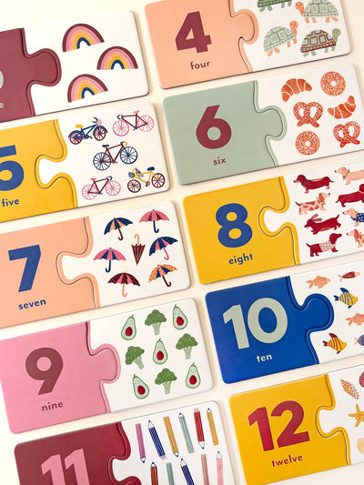 The Lauren Sissons Studio Number Puzzle Pairs is a kids’ educational game featuring cards with numbers (4-12), their names, and fun images like rainbows, bikes, donuts, or cats—ideal for building early counting and numeracy skills.