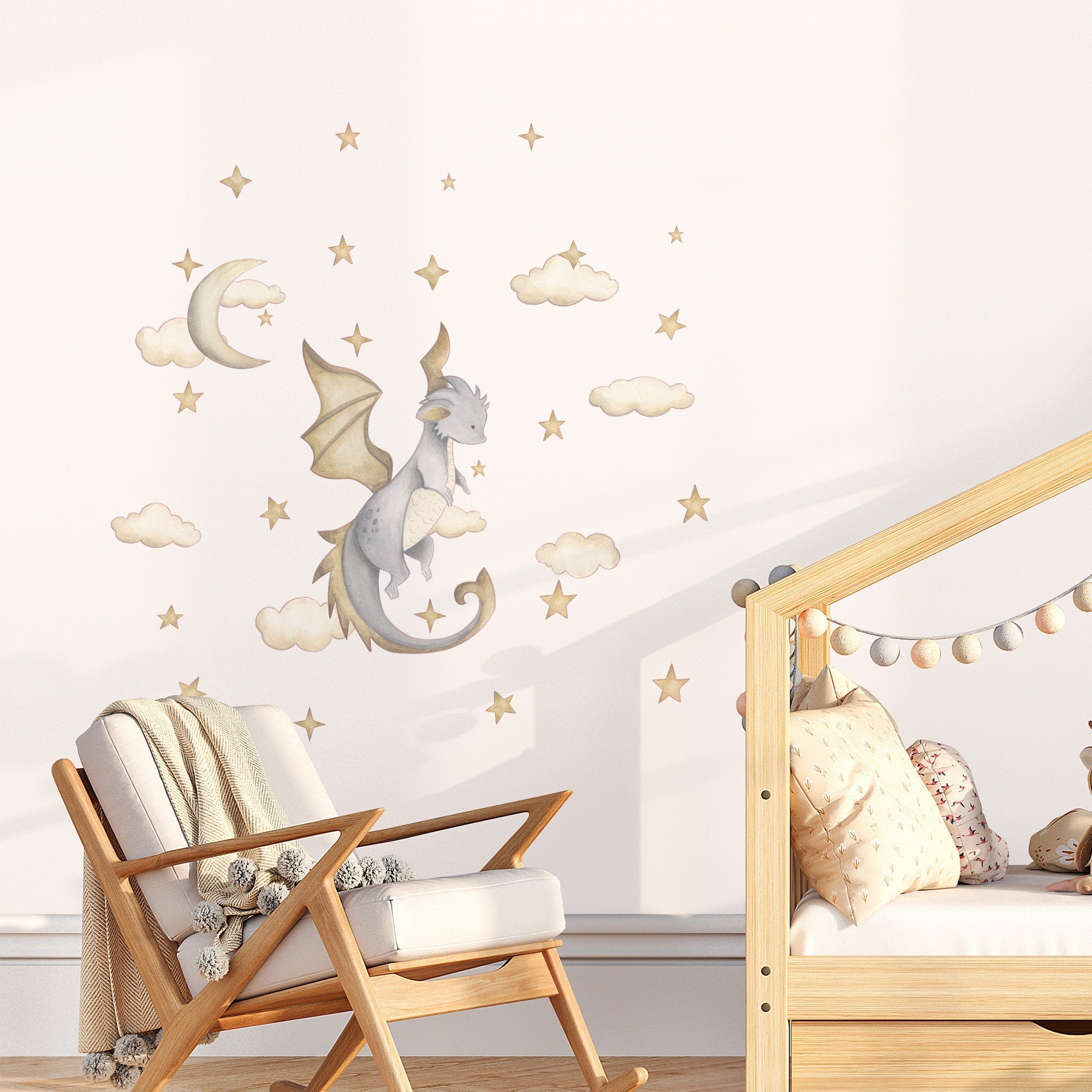 A cozy childrens room with a wooden chair and crib features My Stores Dragon Stickers, including whimsical watercolour dragons, stars, clouds, and a crescent moon on the wall. A fluffy blanket is draped over the chair while a pillow rests in the crib.