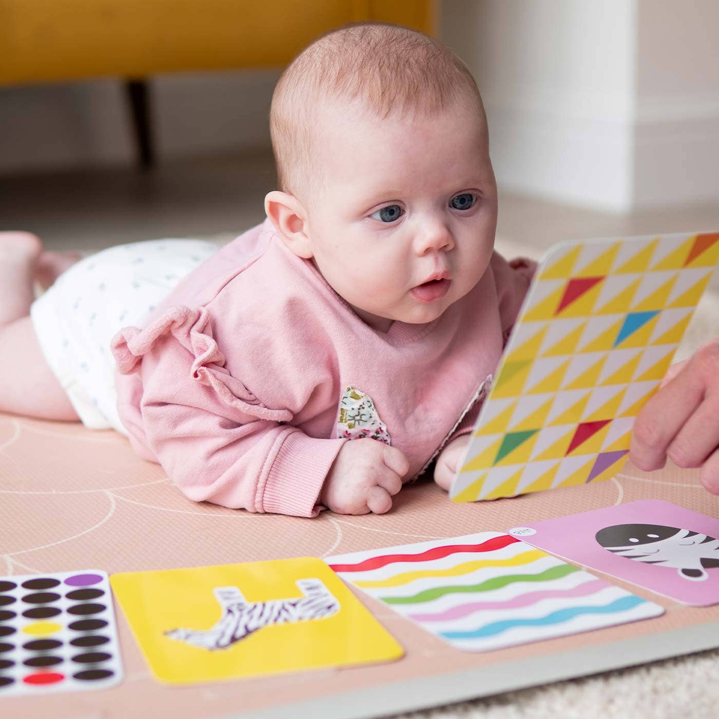A baby lies on their stomach, engaging with Priya & Peanut's Colour Sensory Flash Cards For Babies (3+ Months), a sensory toy featuring bright, contrasting patterns that encourage early development.