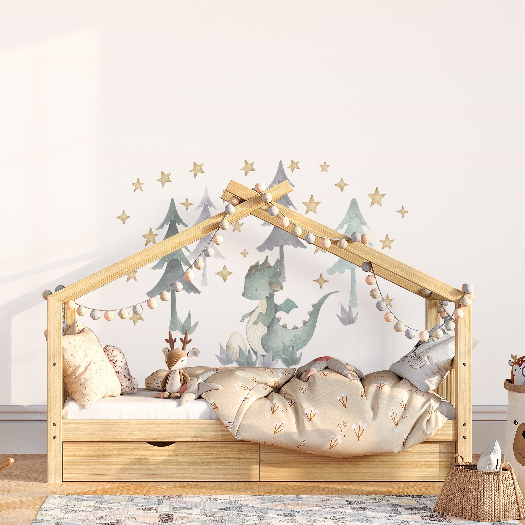 A cozy childrens room features a wooden house-shaped bed adorned with string lights and soft blankets. My Stores Green Dragon Stickers complement the dinosaur mural, surrounded by stars and trees. A stuffed deer toy and woven basket complete the decor with easy-application stickers.