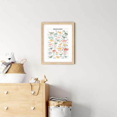 A nursery room features a light wooden dresser with heart-shaped handles and plush toys. A woven basket and My Stores Dinosaur Alphabet Nursery Print adorn the wall, creating an educational, playful, and cozy atmosphere.