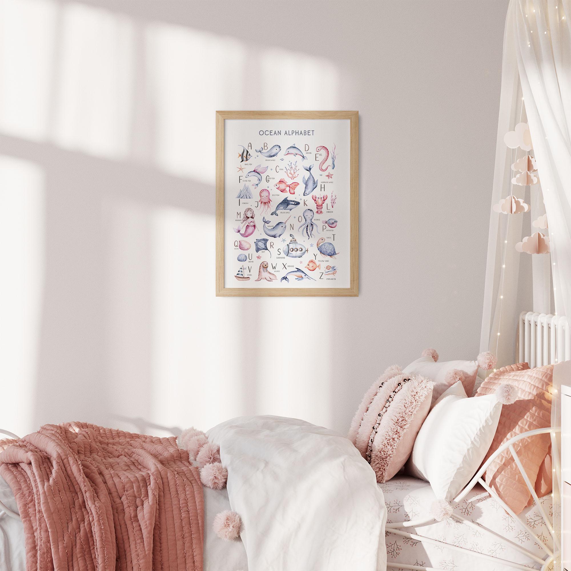 A cozy bedroom showcases a white bed with pink and white pillows, a pom-pom adorned pink throw, and fairy lights above. A framed My Store Under The Sea Nursery Wall Print adds educational charm with its marine life illustrations.