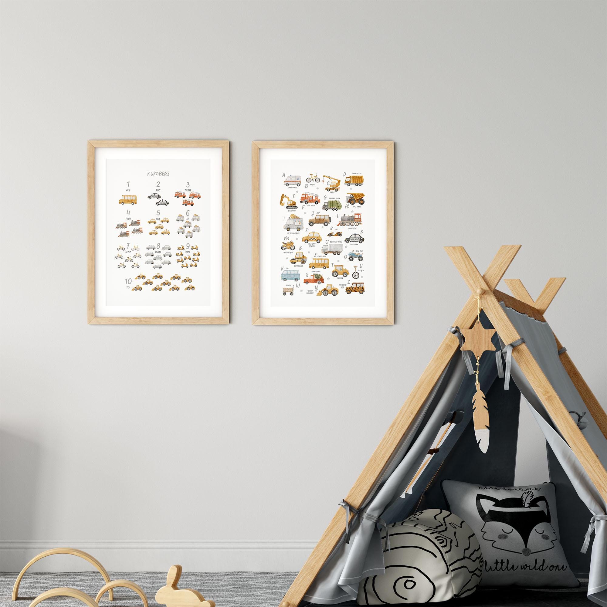 A childrens room with two Transport Alphabet & Numbers prints by My Store on a light gray wall. Nearby, a cozy wooden play tent with decorative elements and pillows invites imaginative play amidst educational designs of vehicles like buses and trucks.