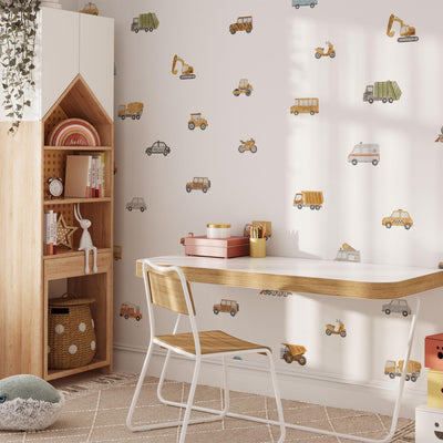 A cozy childrens room features a wooden desk and chair, My Stores Transport Vehicles Wall Stickers, and a house-shaped bookshelf. A basket, plant, and fluffy cushions enhance the playful and inviting atmosphere.