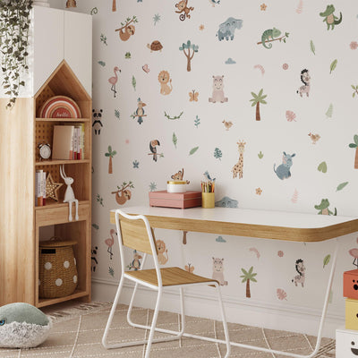 A childrens room features a white desk and wooden chair. The wall showcases My Stores Jungle Animal Wall Stickers with lions, giraffes, and flamingos. A house-shaped wooden shelf holds books and toys, while a plant hangs from the top shelf enhancing the nursery decor.