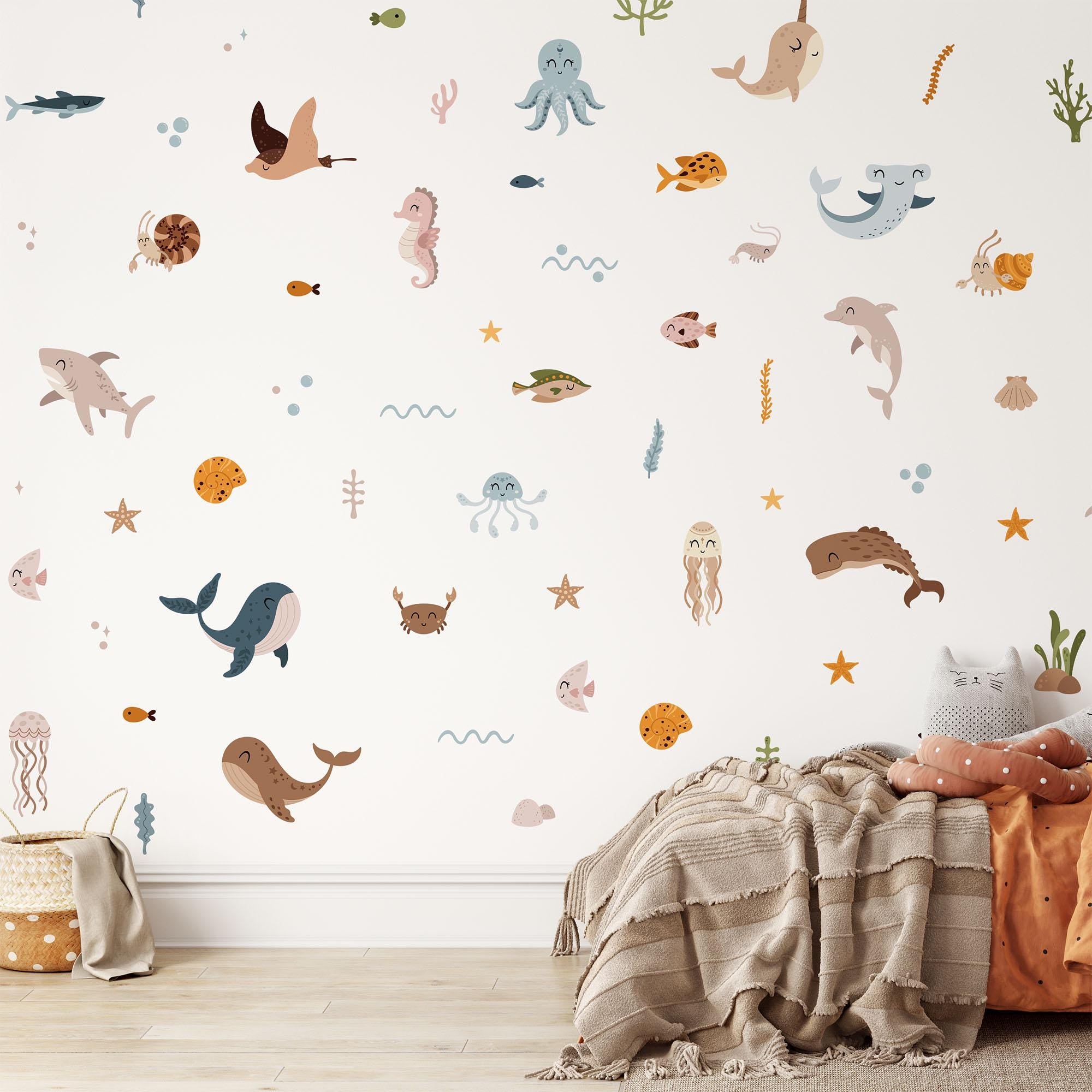 A cozy room features My Stores Ocean Animals Stickers, displaying whales, sharks, octopuses, and dolphins. A soft beige blanket and pillow are on the floor next to a toy basket. The decor is whimsical and child-friendly.