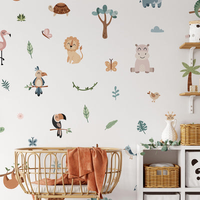The nursery showcases Jungle Animal Wall Stickers from My Store, including a lion, hippo, and flamingo. A round crib with an orange blanket is in the foreground. To the right are shelves filled with stuffed animals and woven baskets, creating a colorful and lively atmosphere.