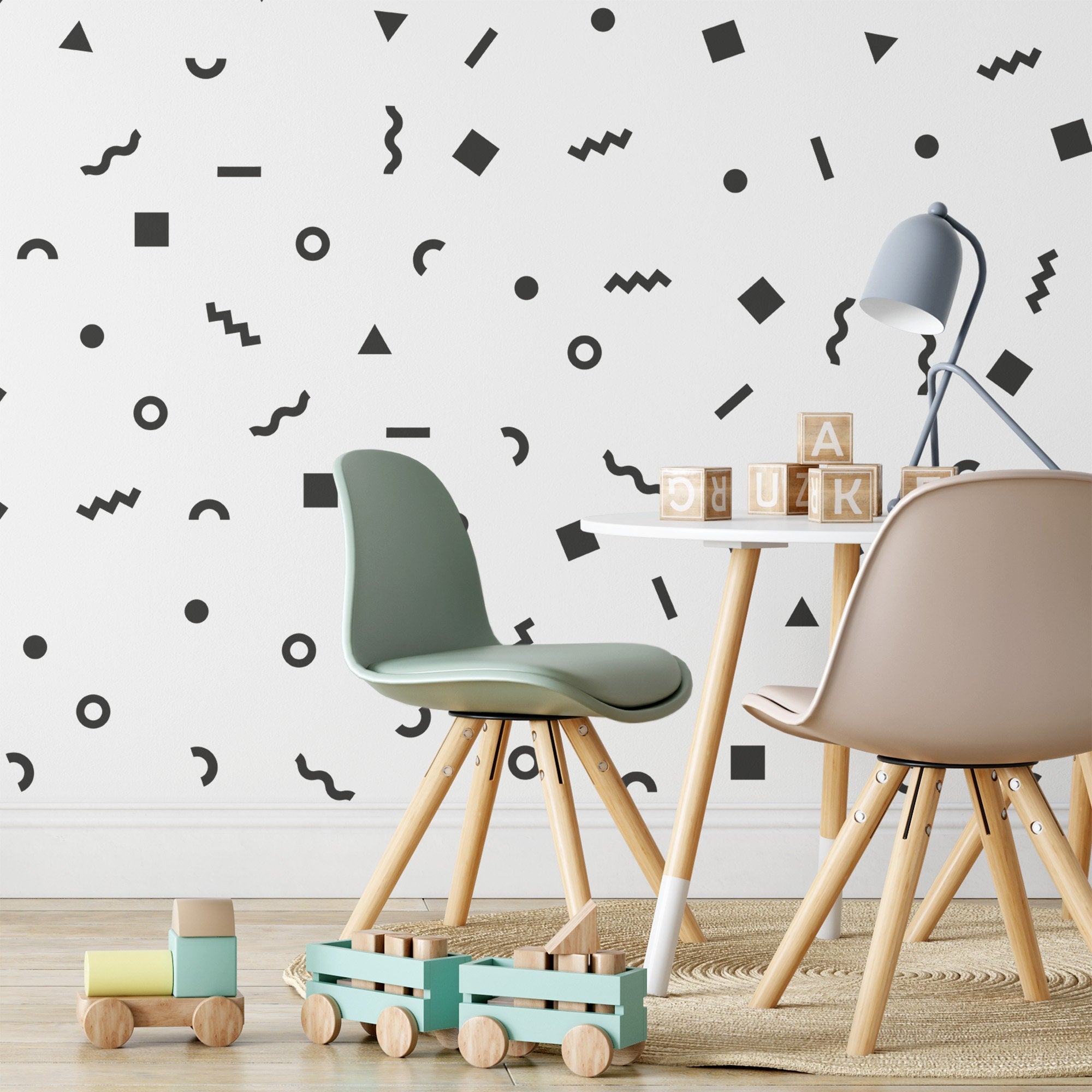 A childrens playroom with two chairs and a small table features My Stores Retro Doodle Stickers, showcasing black geometric shapes on the wall. Wooden blocks and a toy train lay on the floor, while daylight streams in from the side.
