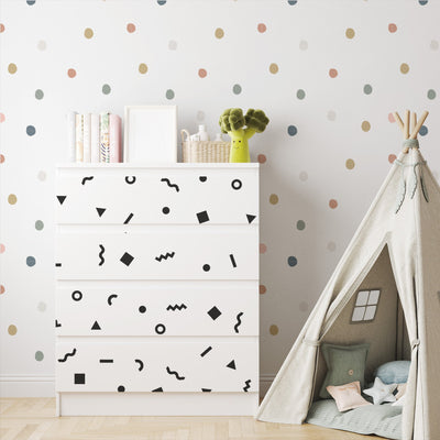 A childrens room includes a white dresser with geometric patterns, a stack of books, and a green toy on top. The wall showcases My Stores Retro Doodle Stickers, while a cozy teepee tent with cushions is arranged on the right.