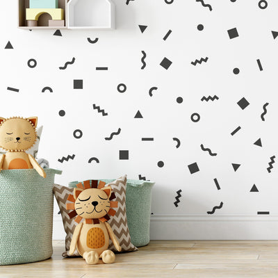 A cozy nursery room features playful wall decals with black geometric shapes. My Stores Retro Doodle Stickers add whimsy, while a cute stuffed lion sits in a basket with a plush lion pillow, adding charm to the space.