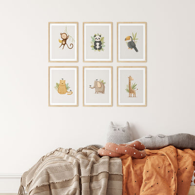 A cozy room showcases My Stores Safari Animals Nursery Prints, a set of six framed pieces above a bed. The bed, with patterned blankets and animal cushions, exudes a playful and warm vibe.