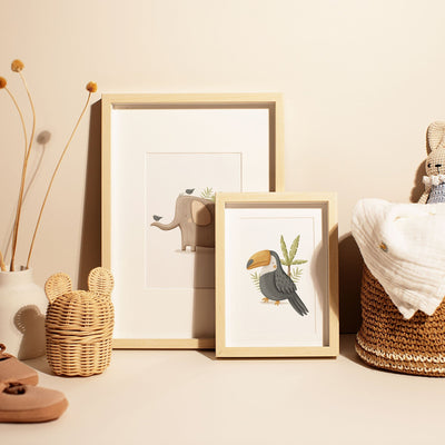 My Stores Safari Animals Nursery Prints, showcasing an elephant and a toucan, adorn a neutral-toned surface. Paired with a woven basket, dried flowers in a vase, and soft baby items, they create a cozy nursery art environment.