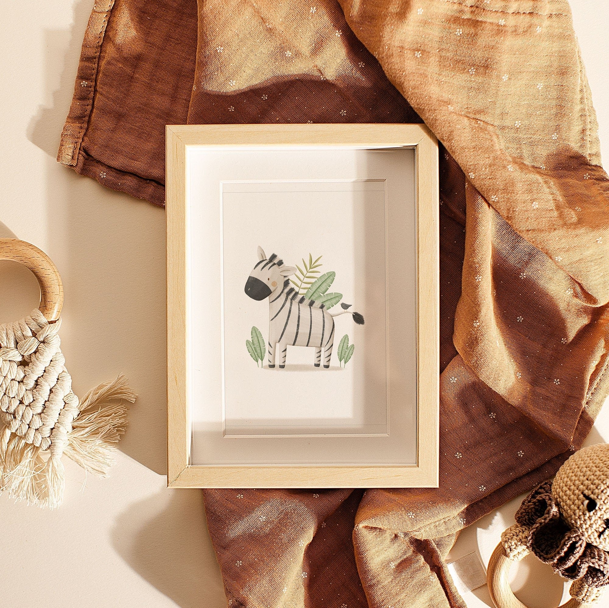 The Safari Animals Nursery Prints by My Store feature a framed zebra illustration showcased with draped brown fabric, macramé, and small woven items against a beige background.