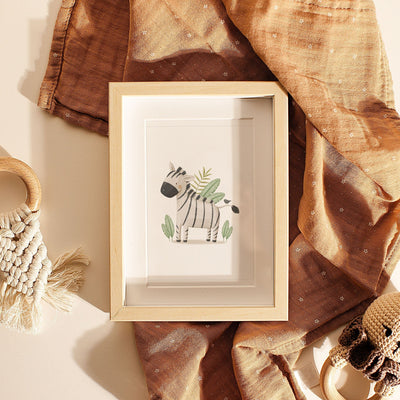 The Safari Animals Nursery Prints by My Store feature a framed zebra illustration showcased with draped brown fabric, macramé, and small woven items against a beige background.