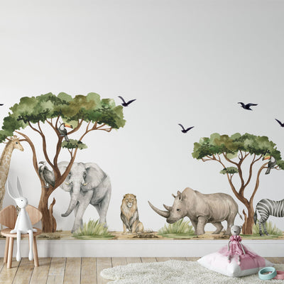 A kids room boasts a vibrant mural of safari animals with Safari Animals Nursery Stickers by My Store—giraffe, elephant, lion, rhinoceros, and zebra under trees. Watercolour decals add charm with flying birds above. A plush rabbit sits on a chair near a doll on a cushion and a toy wagon on the floor.