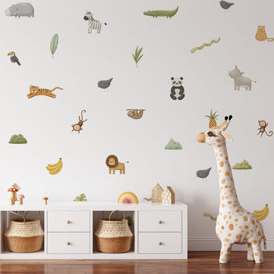 The nursery room displays My Stores Safari & Jungle Animal Stickers, including zebra, lion, panda, and giraffe decals on a white wall. A plush giraffe toy is on the floor next to a white cabinet under the charming stickers.