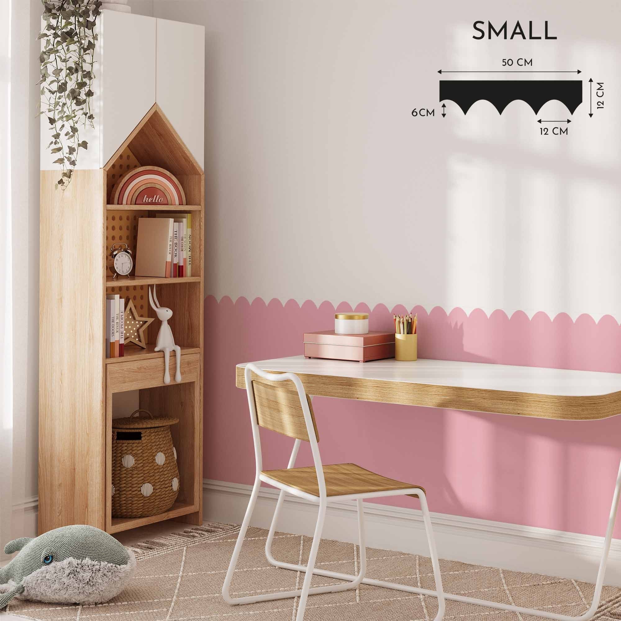 A cozy room includes My Stores Scalloped Wall Stencil to paint a pink accent wall, a wooden desk and chair, and a tall house-shaped shelf for books and decor. A rug and plush toy contribute warmth to the light, airy space.