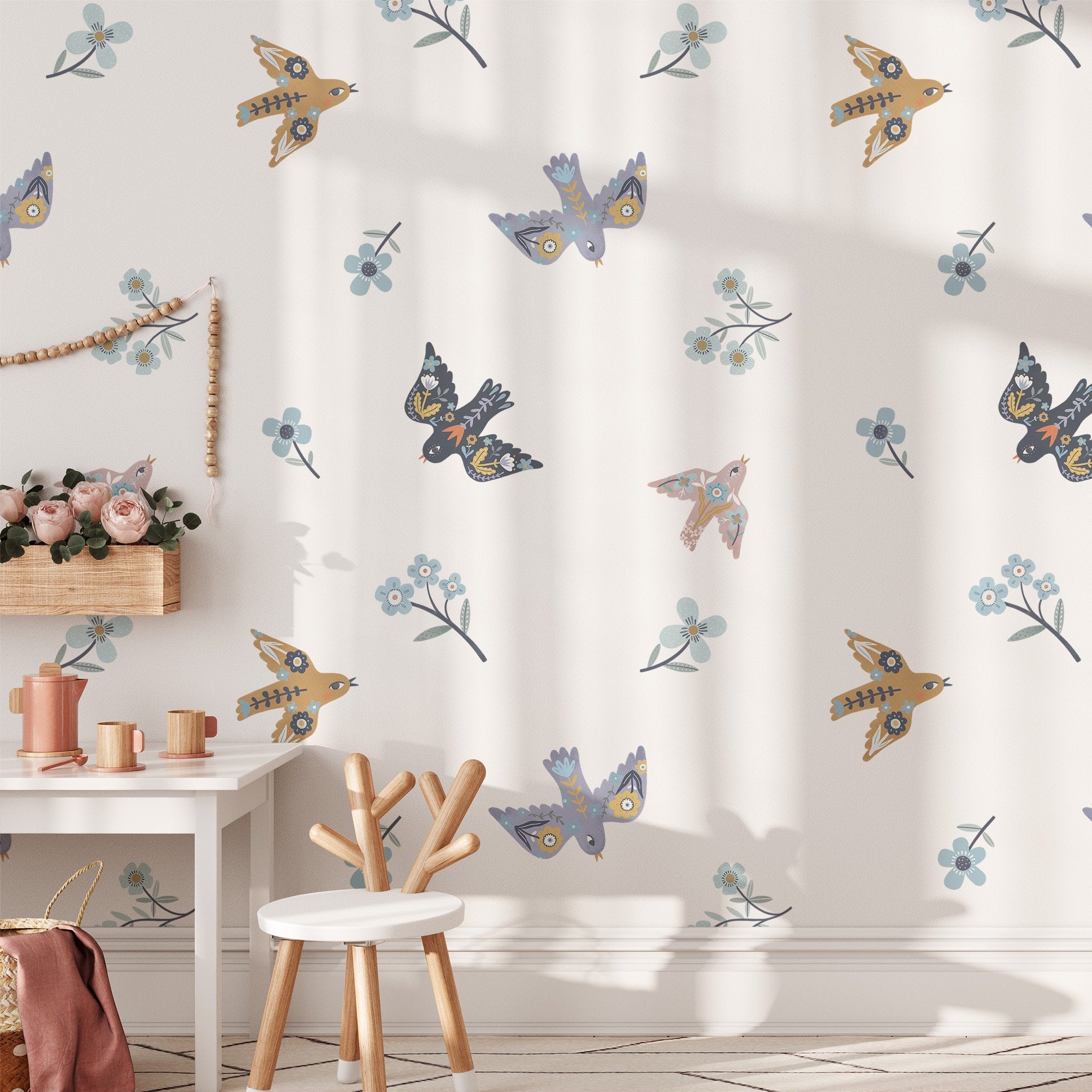 The serene childrens room features white walls decorated with My Stores Summer Mood Wall Stickers, showcasing vibrant bird and floral patterns. A wooden chair and table sit next to a plush toy-filled shelf, adding a cozy touch to the playful nursery setup.