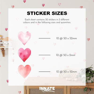 A size chart for My Stores Watercolour Heart Stickers features heart-shaped decals: 10 pink (50x52mm), 10 deep pink (50x2mm), and 10 soft pink (50x52mm). The display includes watercolor heart decor, a plant-adorned shelf, and a wooden cabinet backdrop.