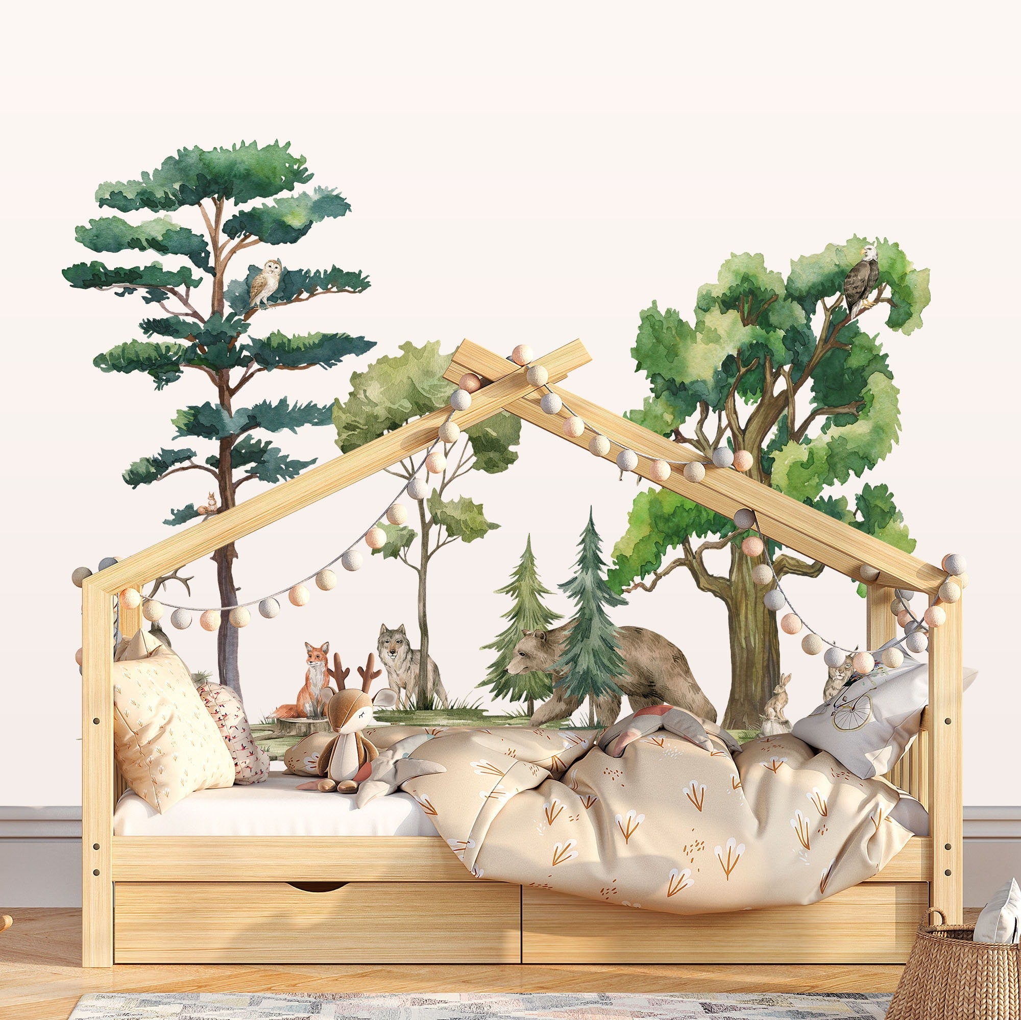 A childrens wooden house-shaped bed is adorned with string lights and pillows. The wall behind features My Stores Woodland Animals Nursery Stickers, with watercolour trees and animals, creating a cozy atmosphere enhanced by removable stickers for easy decorating.