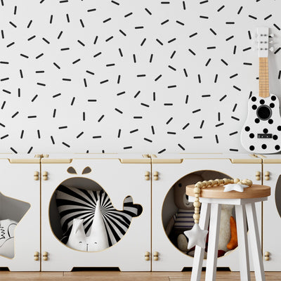 A childs room showcases My Stores Black Sprinkle Stickers on a white wall. A guitar is mounted on the wall, and wooden storage cubes store a zebra toy, teddy bear, and beads—ideal nursery decor that balances playful charm with functional storage.