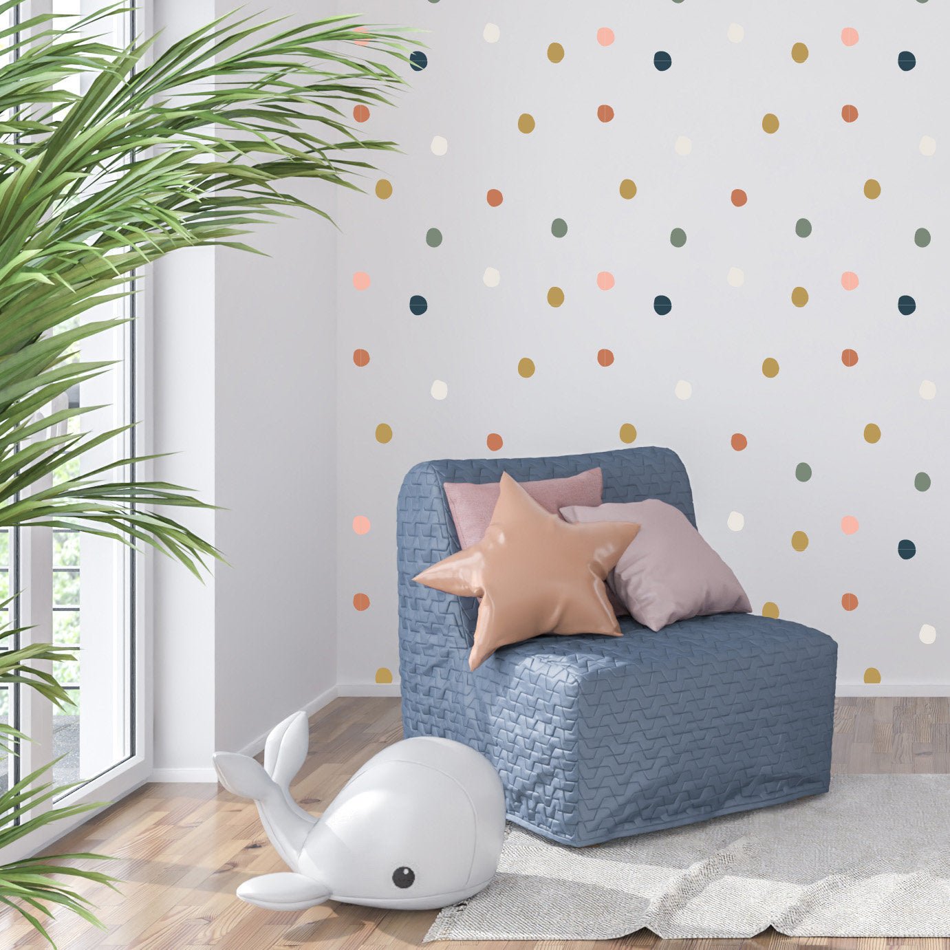 A cozy room features a blue quilted chair with star and round cushions. A plush toy whale lies by a large window. My Stores Coloured Dot Stickers decorate an accent wall, adding charm, while a green plant brings freshness.