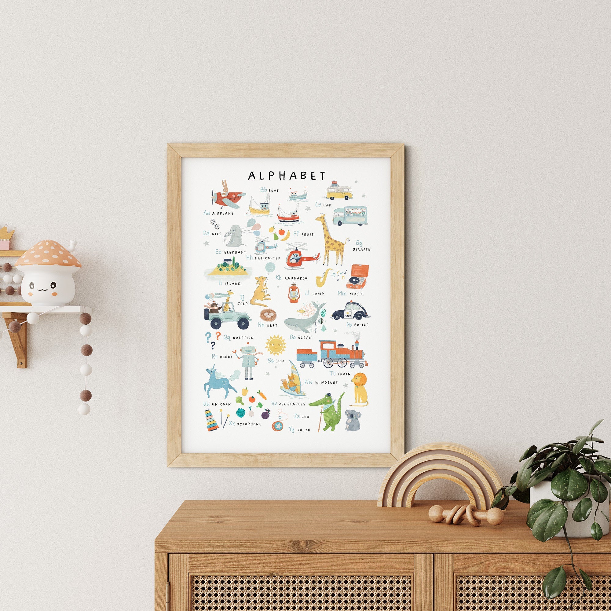 The Numbers & Alphabet Nursery Print by My Store adds educational value as nursery art, showcasing illustrated animals and objects for each letter. It hangs on a light wall above a wooden cabinet, with a shelf featuring a cute toy and small potted plant enhancing the scene.